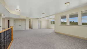 Spacious bonus room featuring neutral carpeting, multiple windows, a wood and wrought iron railing, and recessed lighting
