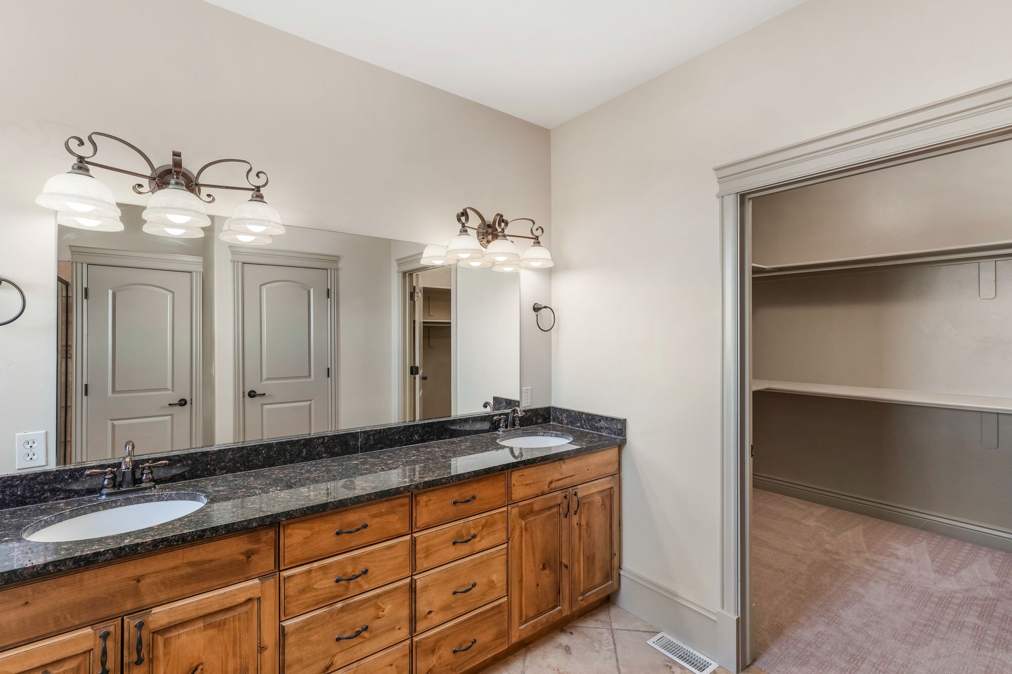 Double vanity featuring wood cabinetry, dark speckled countertop, dual undermount sinks, and bronze-finish fixtures