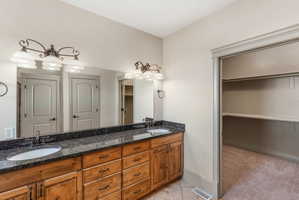 Double vanity featuring wood cabinetry, dark speckled countertop, dual undermount sinks, and bronze-finish fixtures