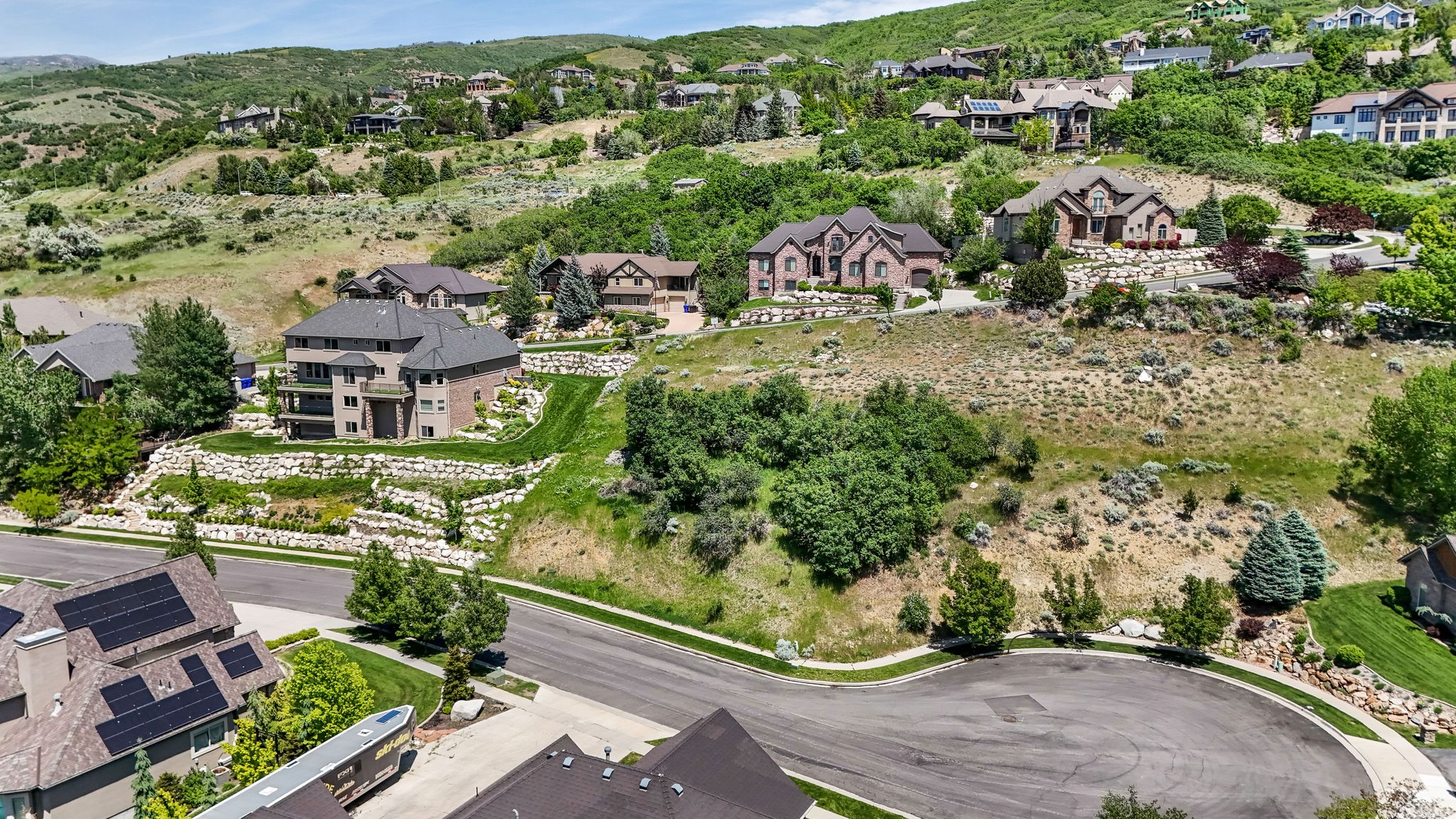 Expansive residential setting featuring multiple homes on terraced lots, surrounded by natural hillside landscaping