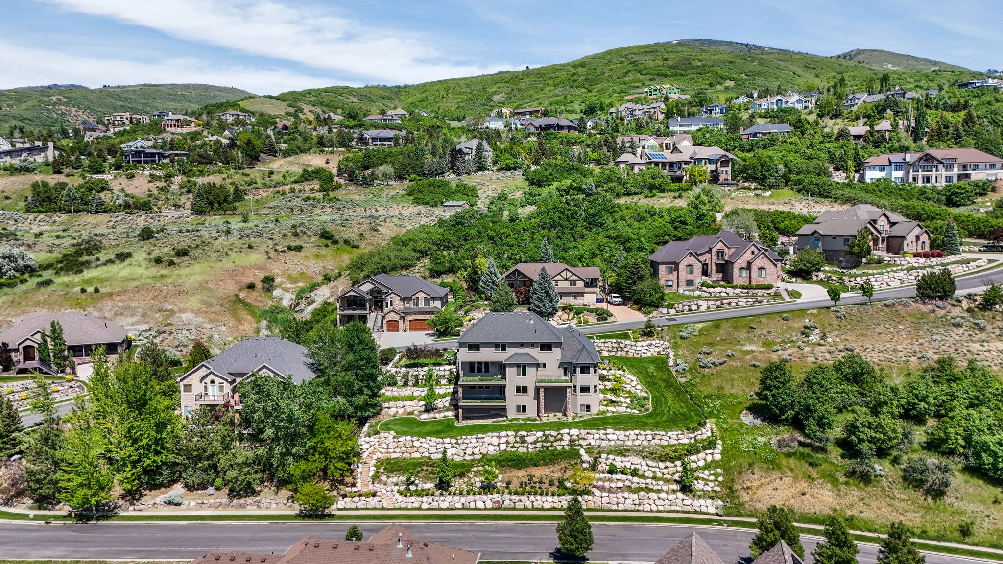 Elevated hillside residence featuring a multi-level design with stone retaining walls, extensive landscaping, and a broad upper-level balcony