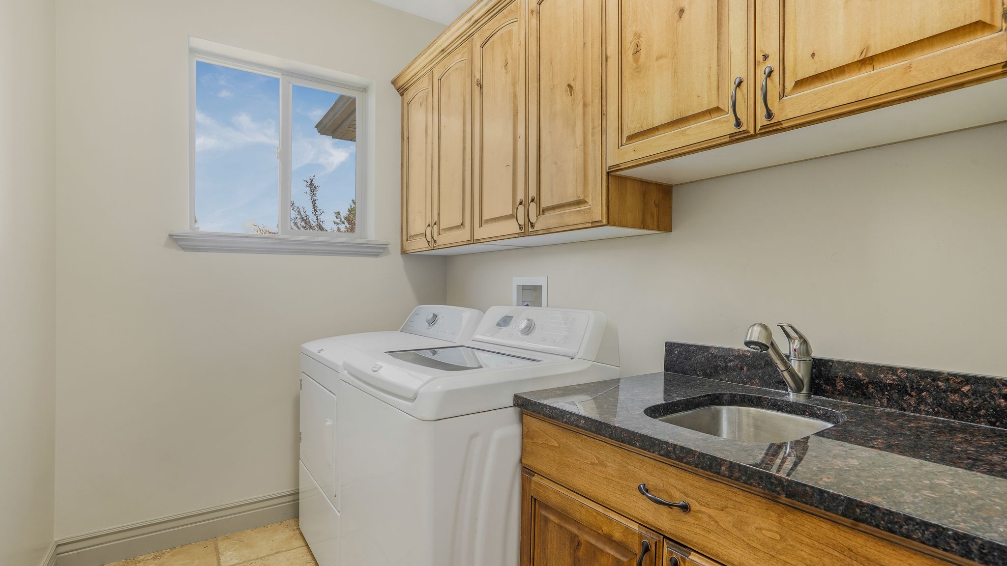 Utility room featuring a window, built-in cabinetry, dark stone countertop, undermount sink, and tiled flooring