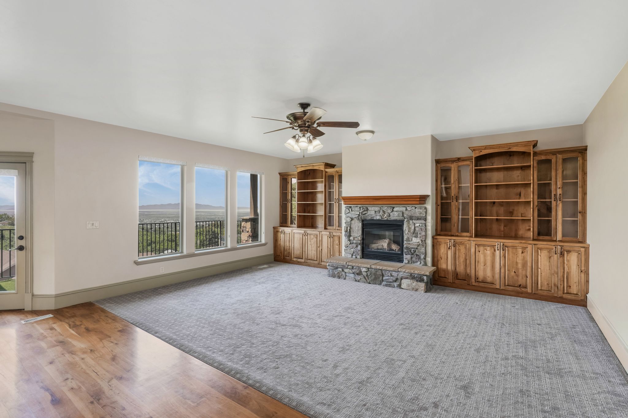 Spacious living area featuring a stone fireplace with a wood mantle, built-in wooden cabinetry, and large windows with exterior access