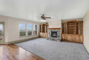 Spacious living area featuring a stone fireplace with a wood mantle, built-in wooden cabinetry, and large windows with exterior access