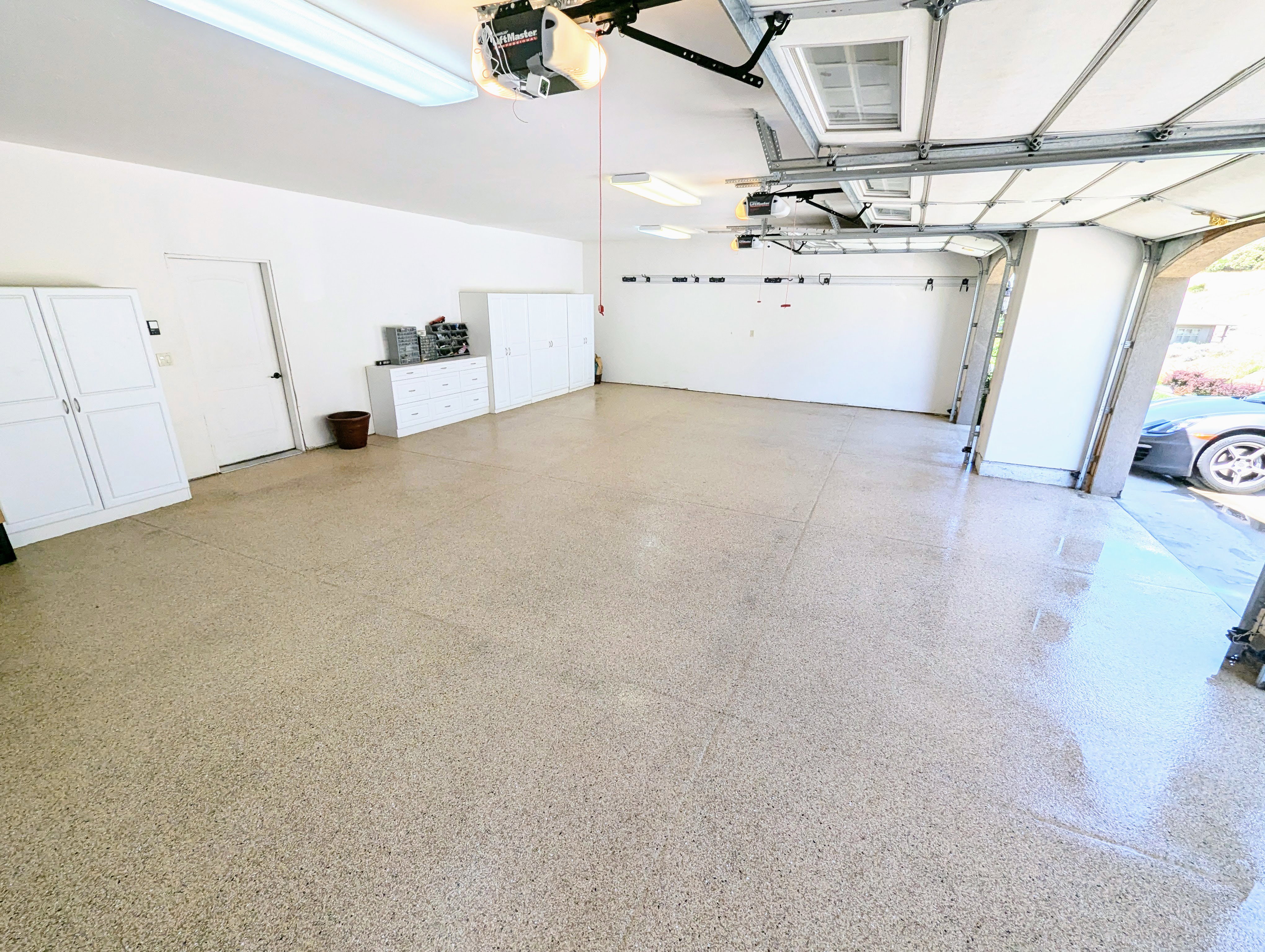 Spacious garage featuring epoxy flooring, overhead lighting, multiple built-in storage cabinets, and a white access door