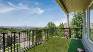 Covered balcony featuring artificial turf flooring, black metal railings, a stone-clad column, and large windows