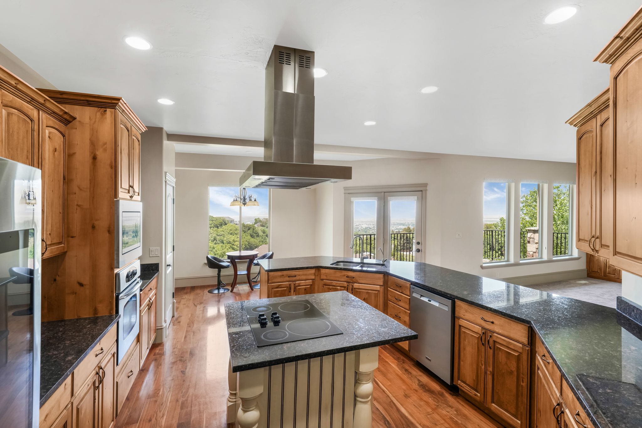 Kitchen featuring a central island with cooktop, granite countertops, wood-finish flooring, light wood cabinetry, and stainless steel appliances