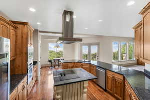 Kitchen featuring a central island with cooktop, granite countertops, wood-finish flooring, light wood cabinetry, and stainless steel appliances