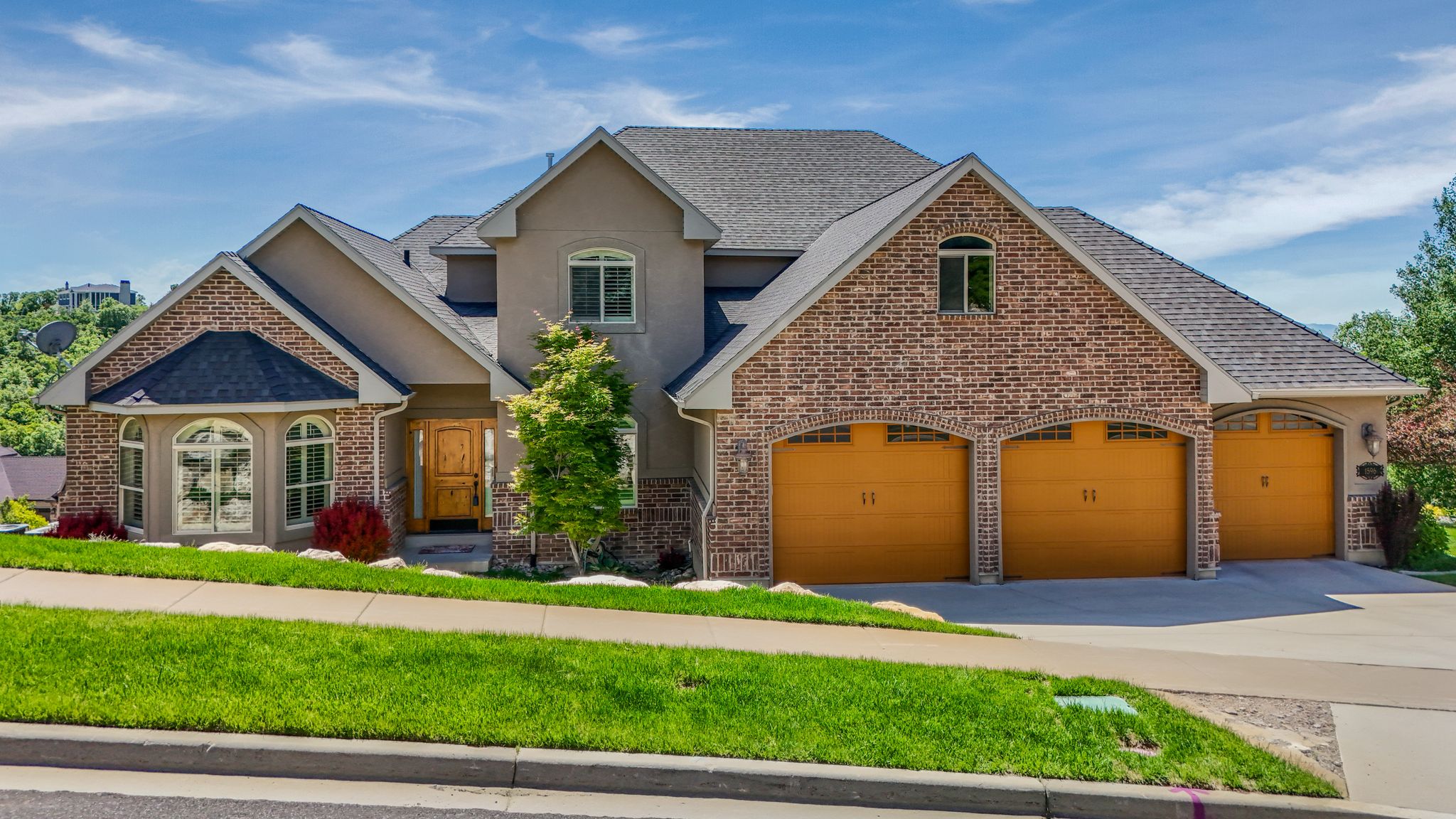 Multi-level residence featuring a brick and stucco exterior, a prominent three-car garage with arched entrances, and a gabled roofline