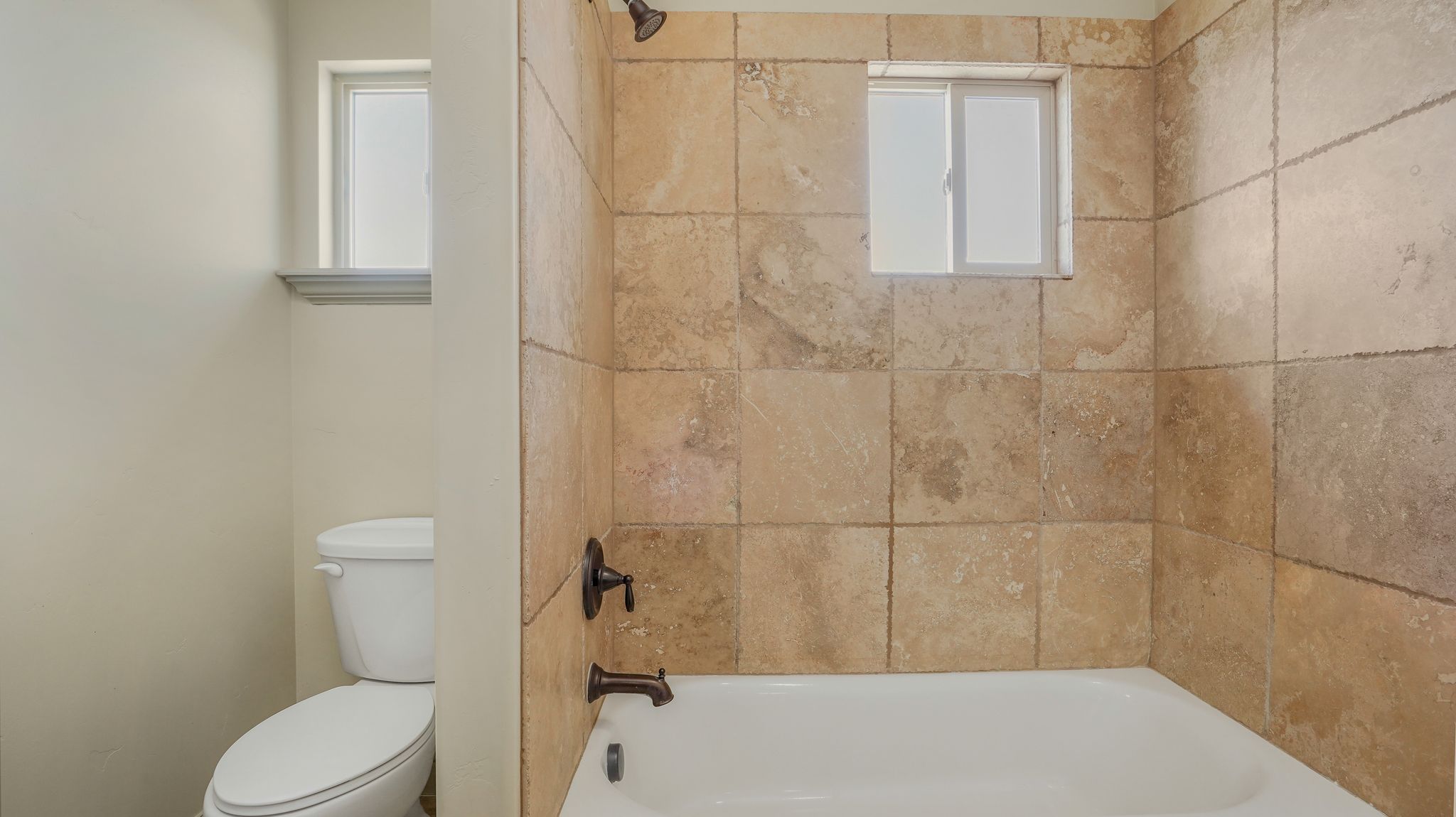 Bathtub with full-height natural stone-finish wall tiling, bronze-finish fixtures, and integrated shower head