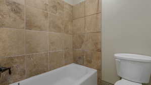 Full bathtub with a bronze-finish fixture, surrounded by large format beige wall tiles and neutral painted walls