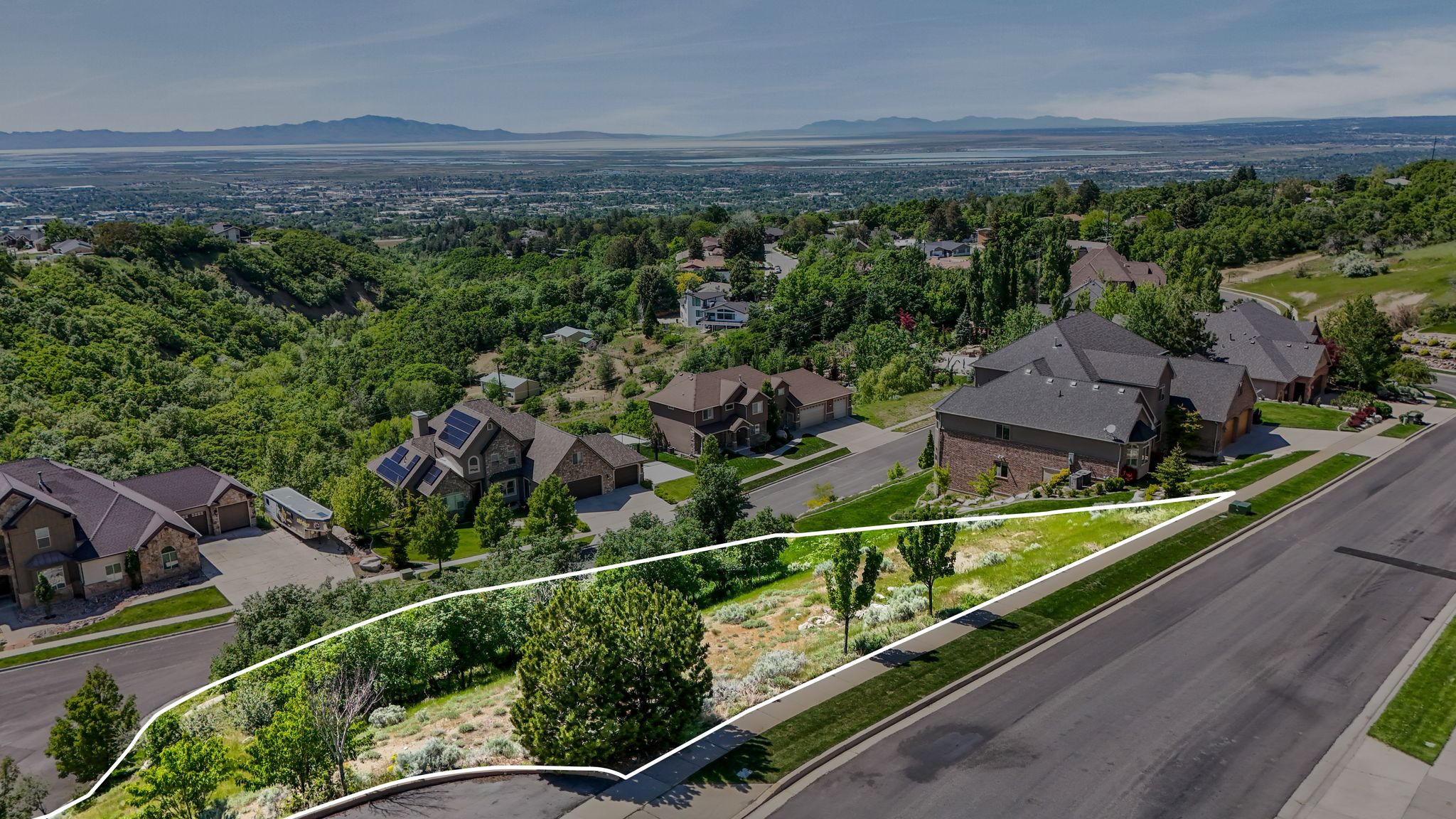 Elevated parcel featuring a paved street frontage, mature and developing trees, and a distant cityscape and mountain backdrop