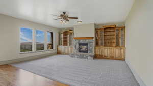 Spacious living area featuring a stone fireplace with a wood mantle, built-in wooden cabinetry, a ceiling fan with integrated lighting, and multiple windows revealing distant mountains