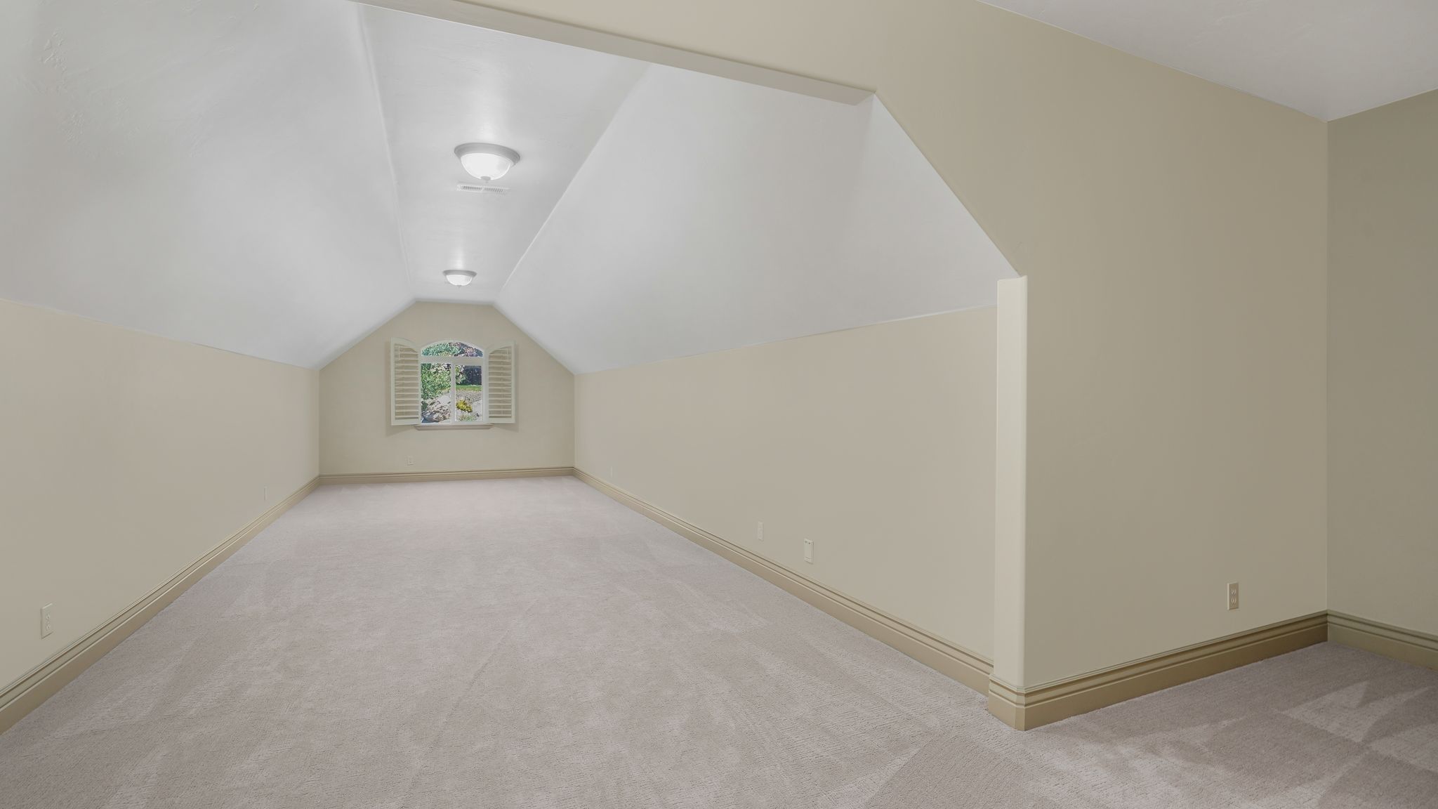 Spacious room featuring vaulted ceilings, plush carpet flooring, recessed wall niche, and natural light from a window with plantation shutters
