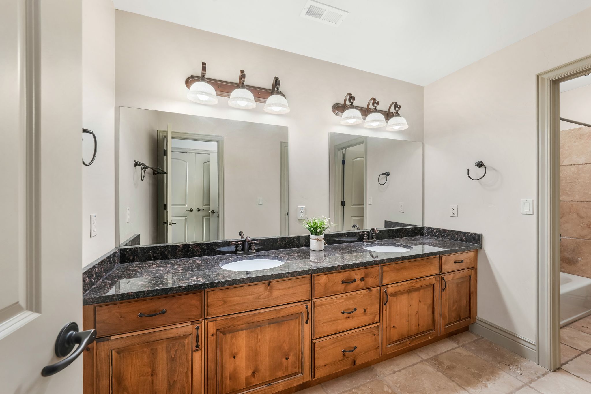 Double vanity with wood-finish cabinetry, granite countertop, dual undermount sinks, and matte black fixtures