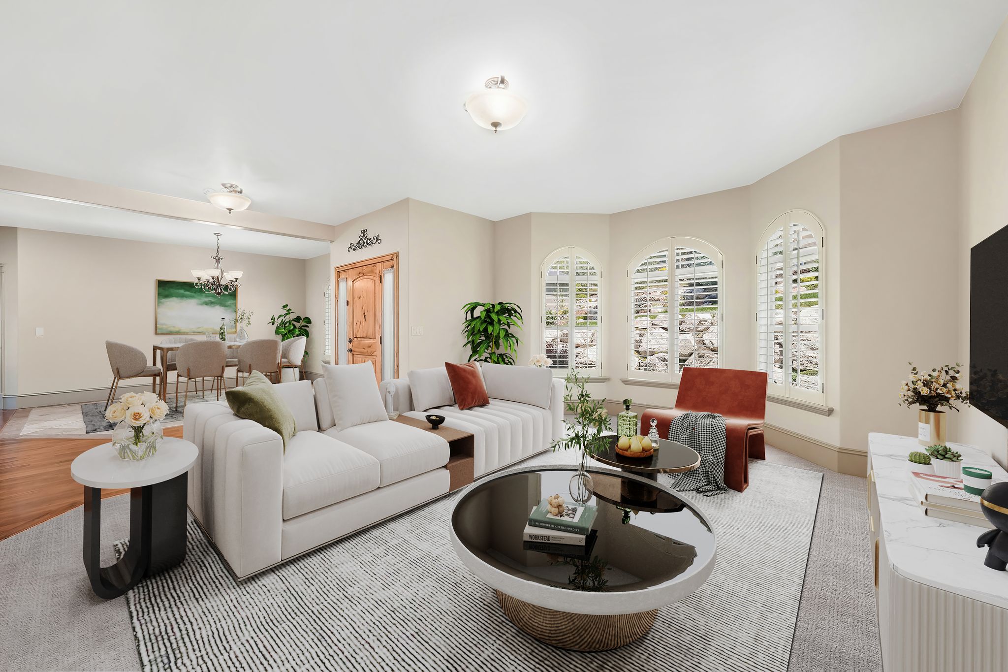 Spacious living area featuring a rounded bay window with arched tops and white plantation shutters, cream-colored walls, and a recessed ceiling light fixture