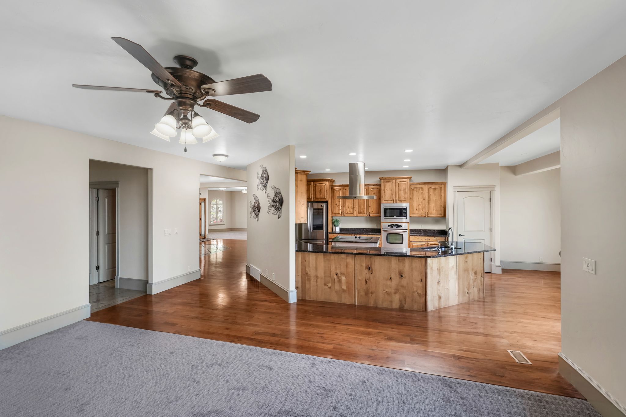 Open-concept kitchen featuring wood cabinetry, stainless steel appliances, dark countertops, and a wood-paneled island with a breakfast bar