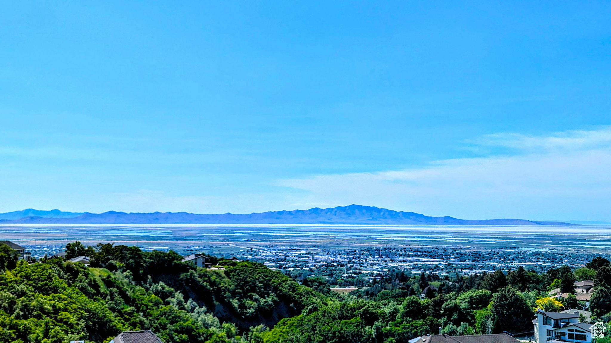 Expansive scenic landscape featuring distant mountains, a large body of water, and a residential area with varied rooflines
