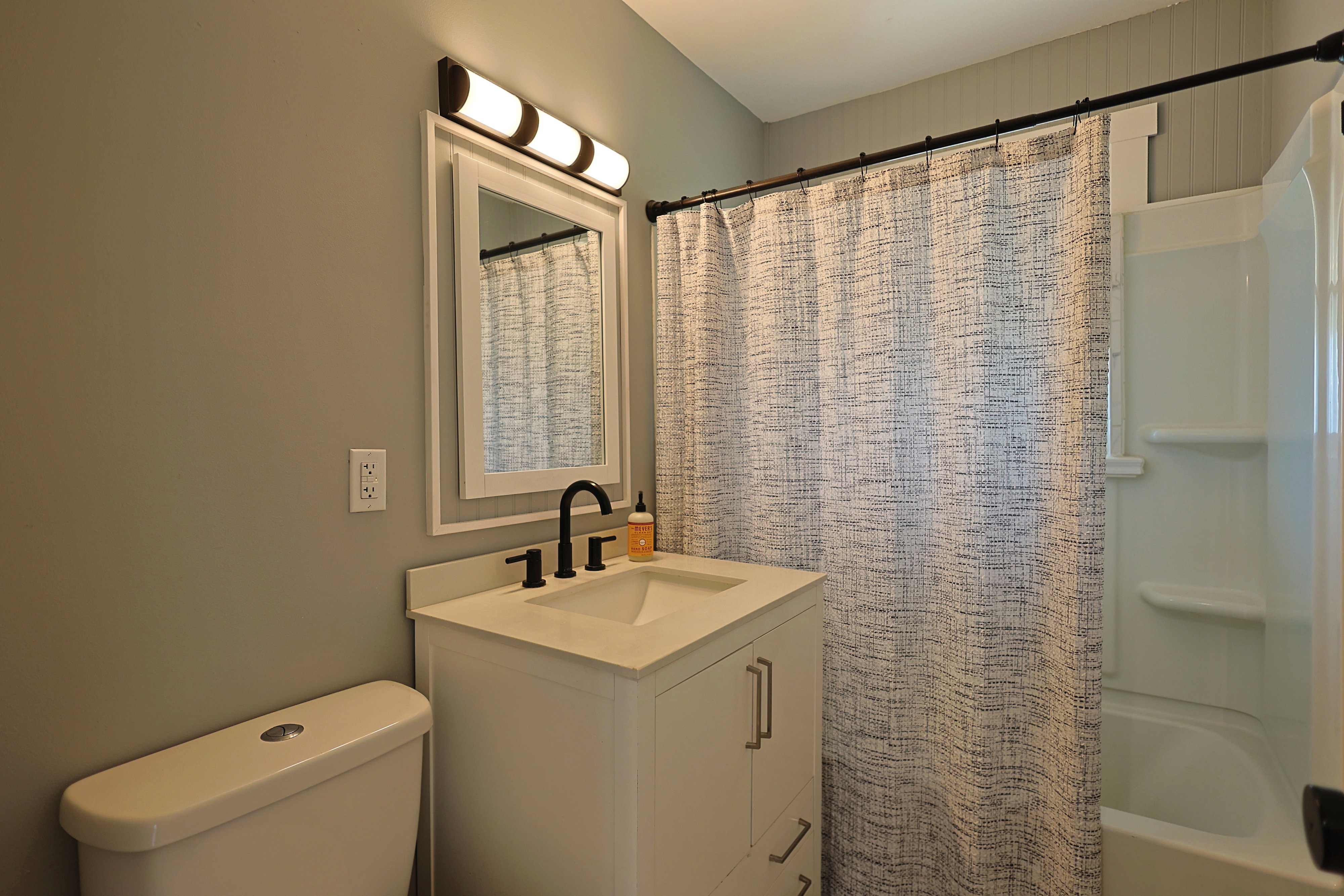 Bathroom featuring a white vanity with an integrated sink, black hardware, framed mirror, and a full bathtub with shower surround
