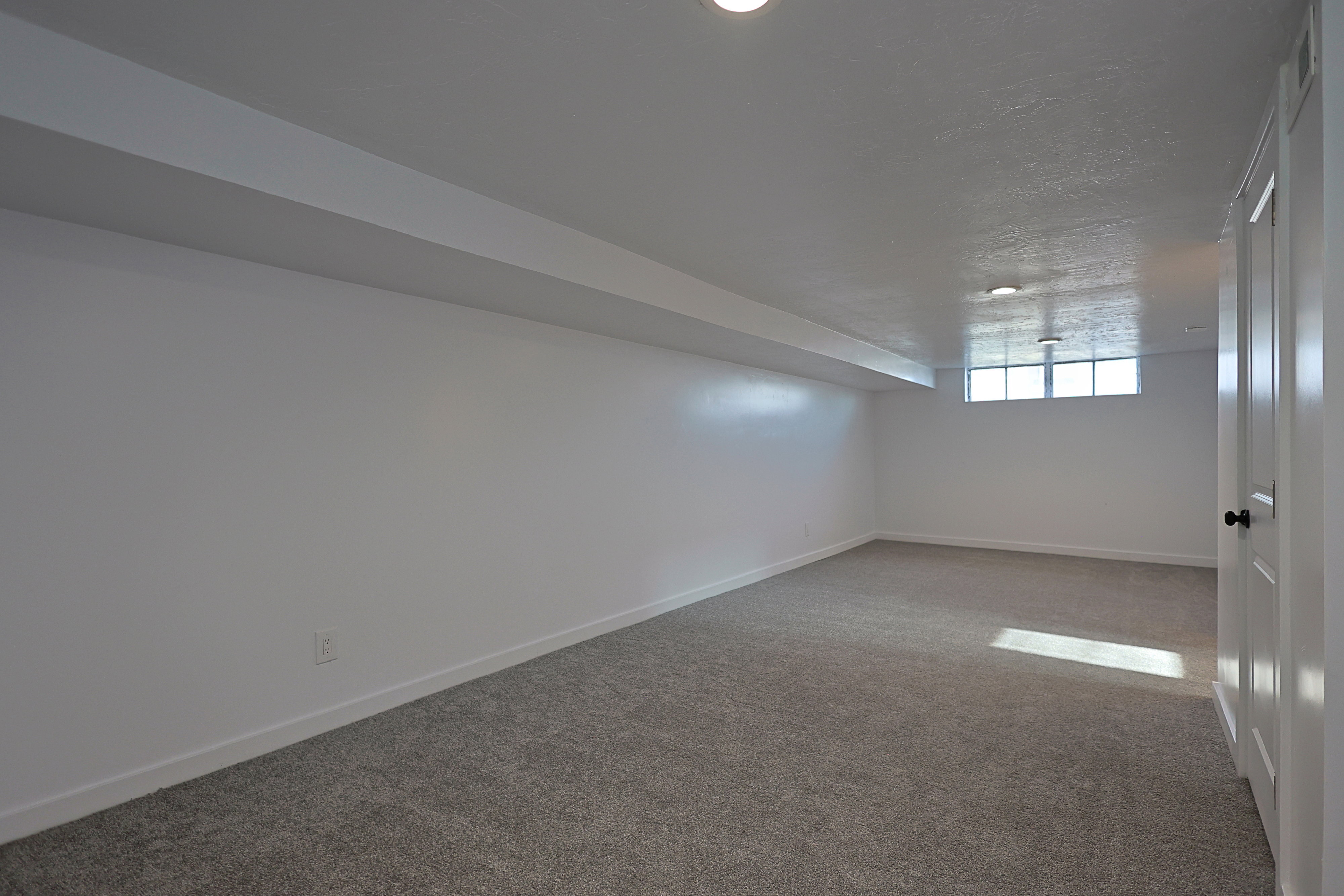 Spacious family room featuring neutral carpet flooring, light-toned walls, recessed lighting, and a window providing natural light