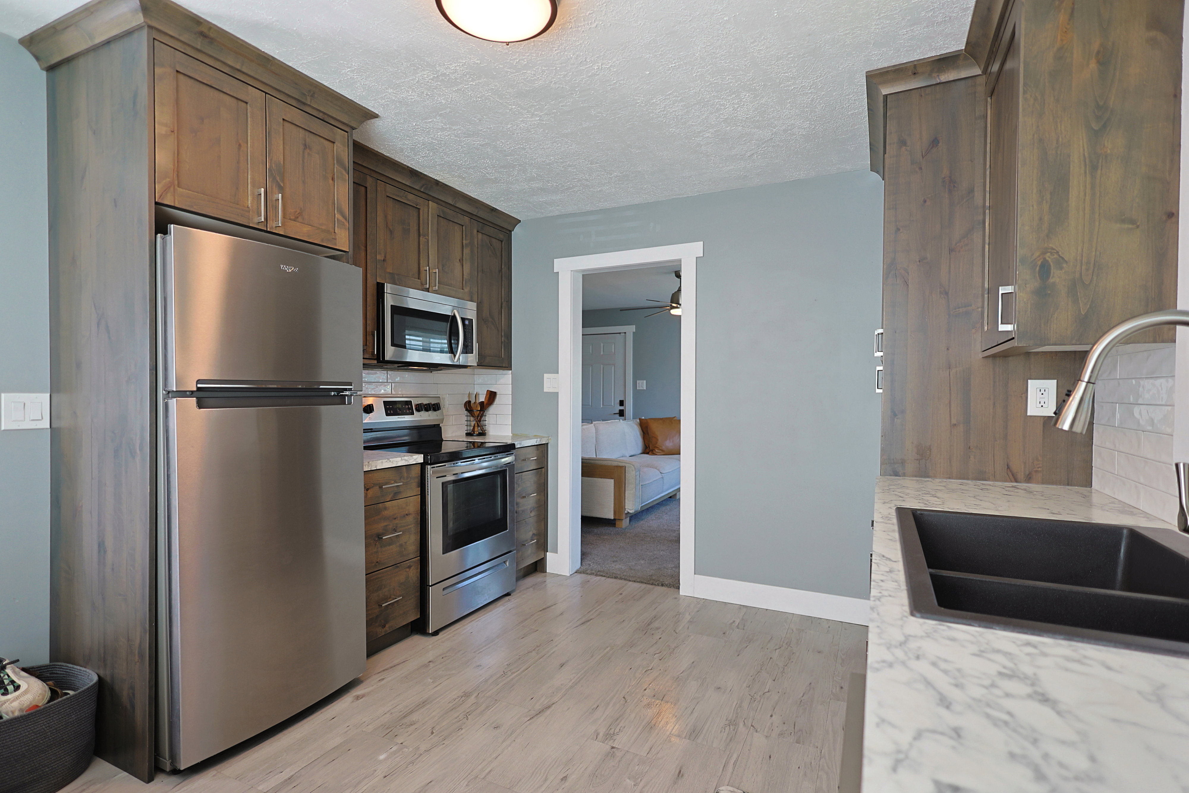 Kitchen featuring wood-finish cabinetry, stainless steel appliances, light wood-look flooring, a white subway tile backsplash, and a black undermount sink