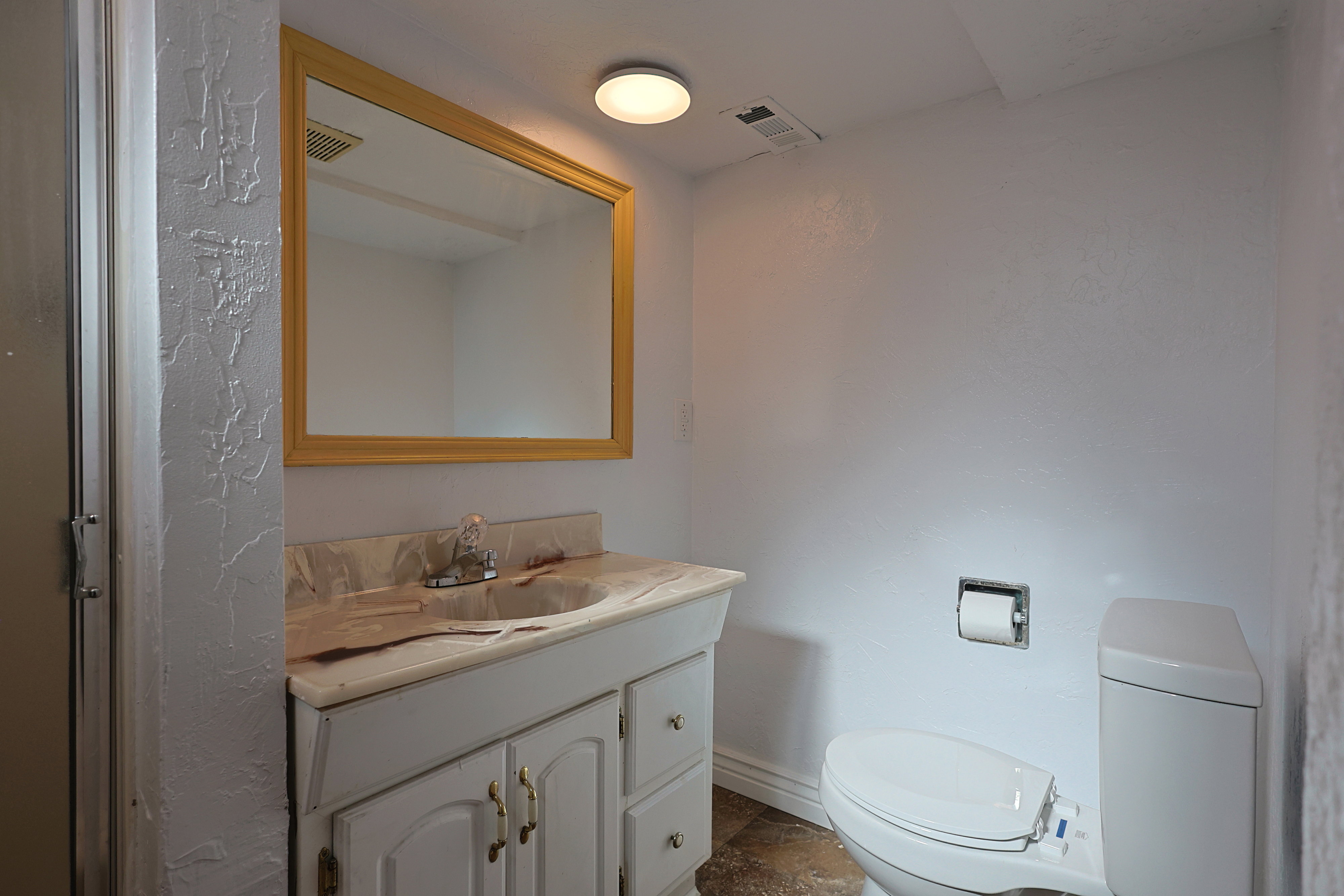 Bathroom featuring a single vanity with a light-colored countertop and a gold-framed mirror