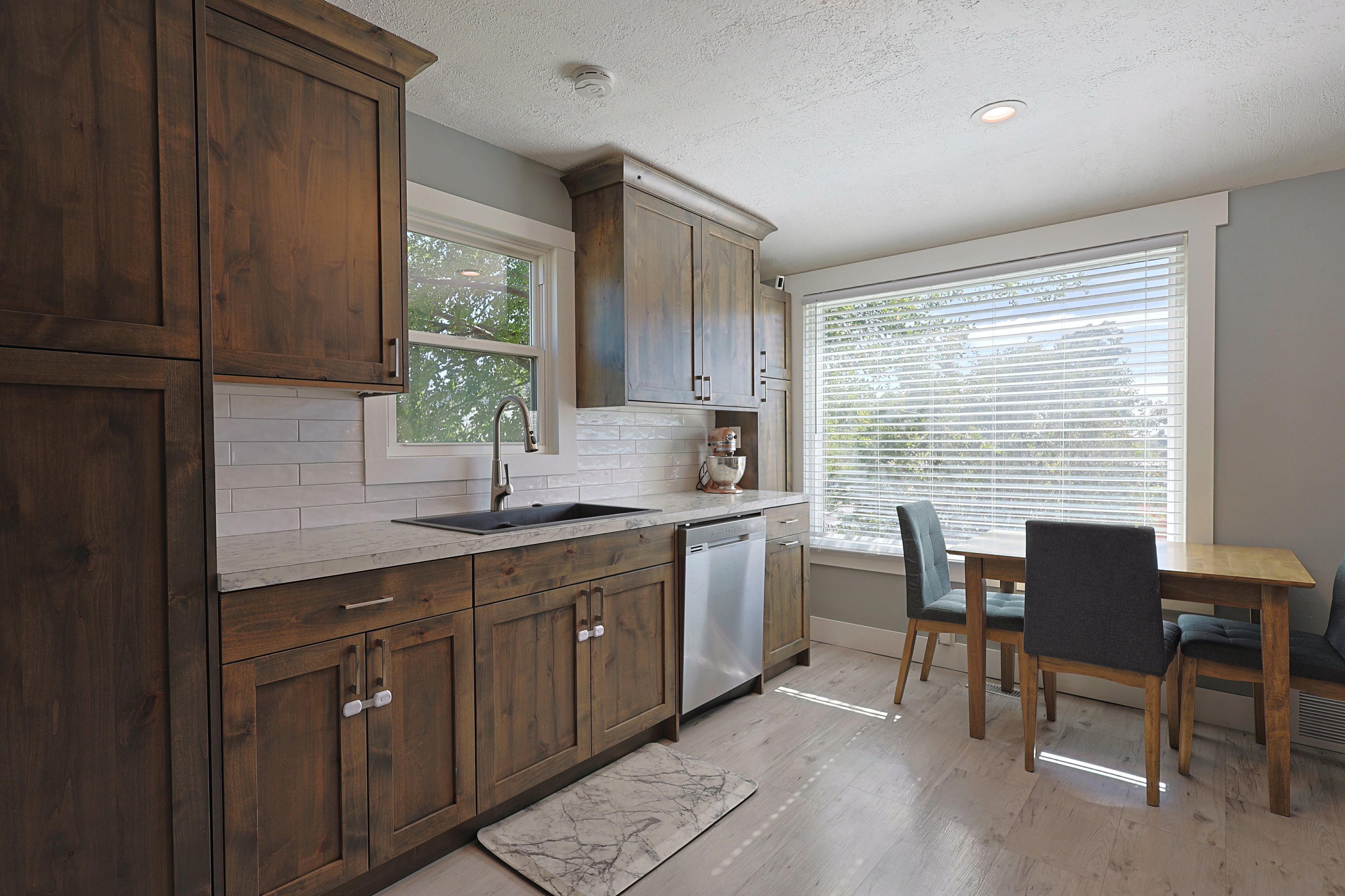 Kitchen featuring wood cabinetry, white subway tile backsplash, light-toned countertops, and stainless steel dishwasher