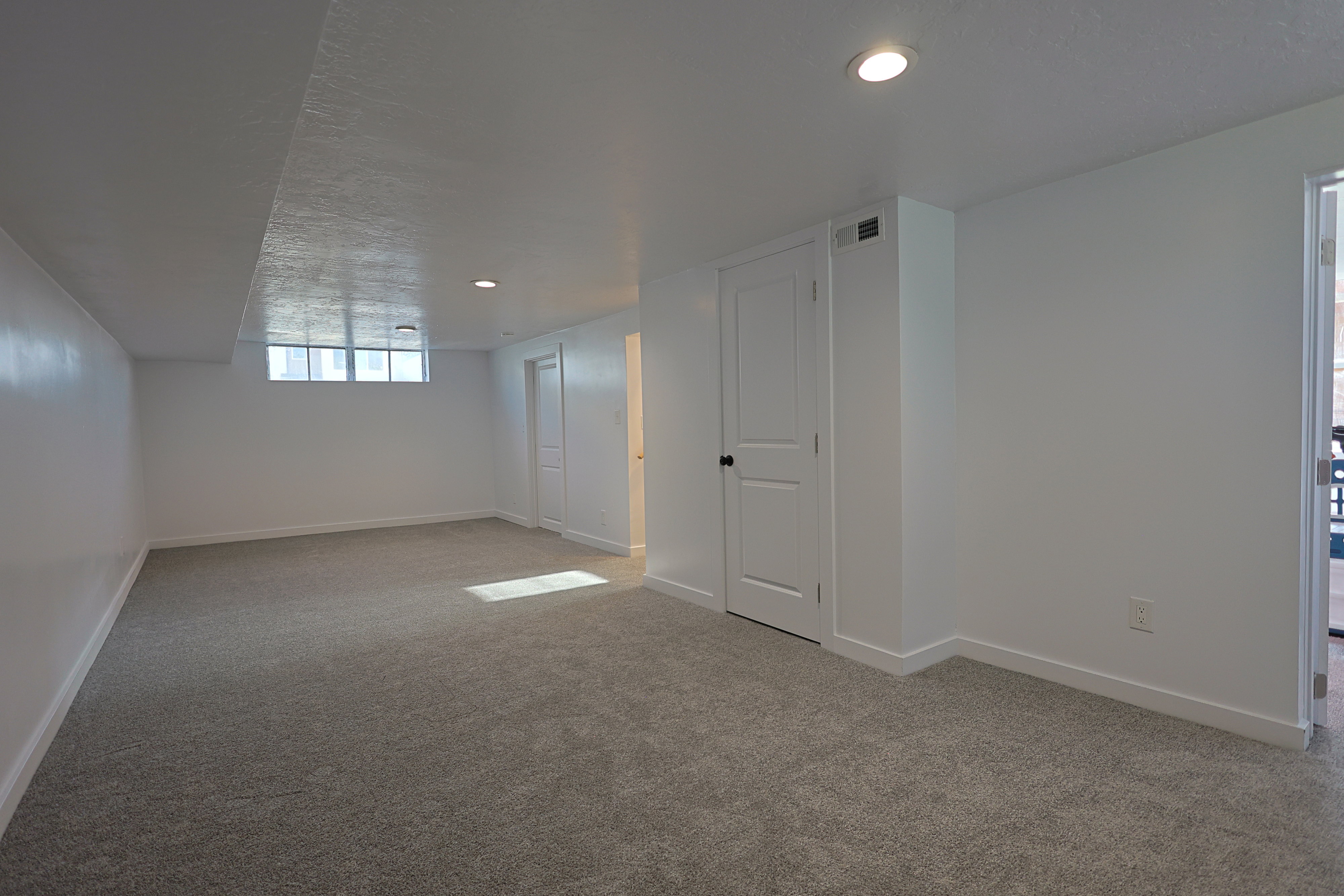 Spacious family room featuring neutral carpeting, recessed ceiling lighting, a window providing natural light, and a white paneled door with dark hardware