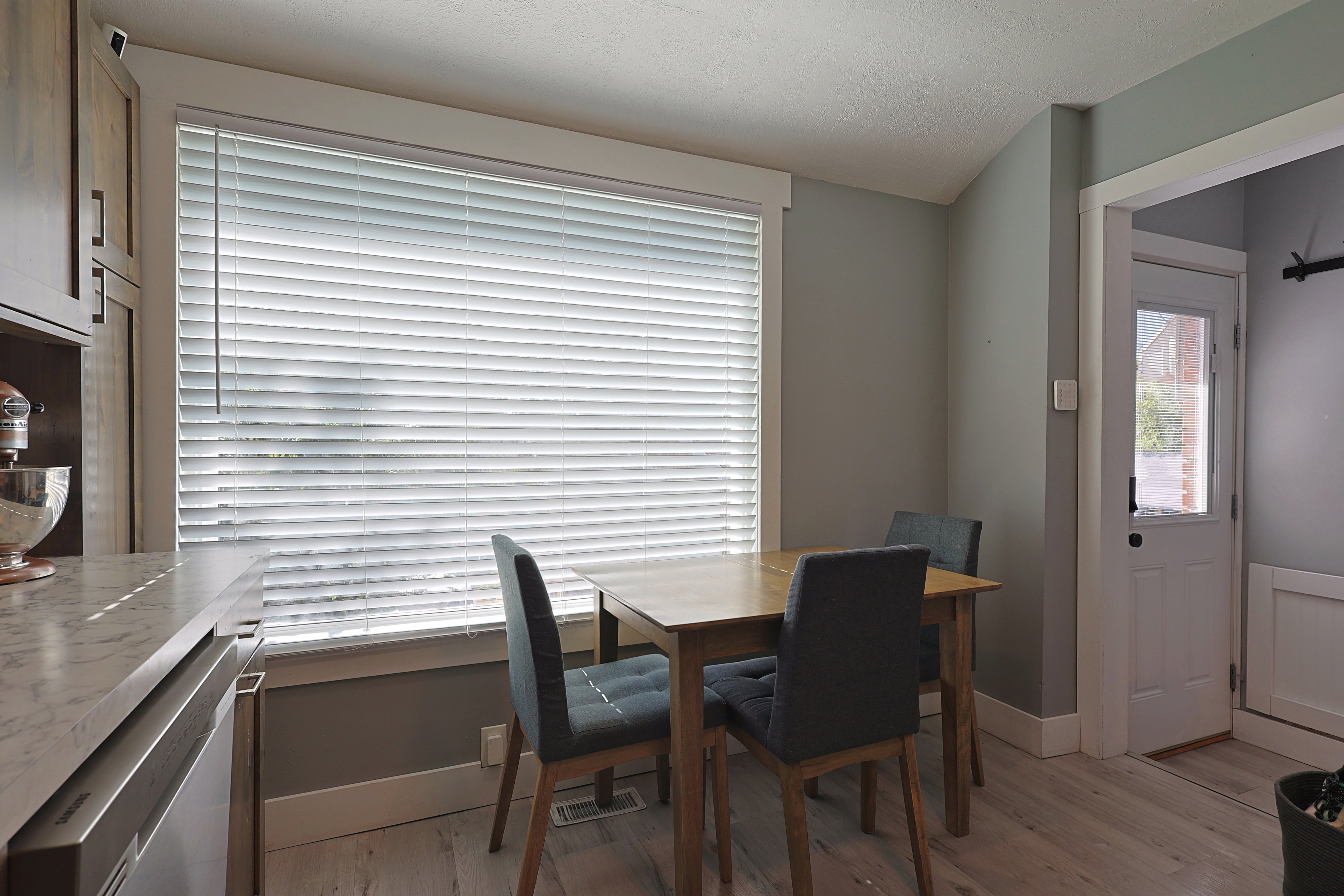 Kitchen dining area featuring wood-finish flooring, light grey painted walls, and a large window with horizontal blinds
