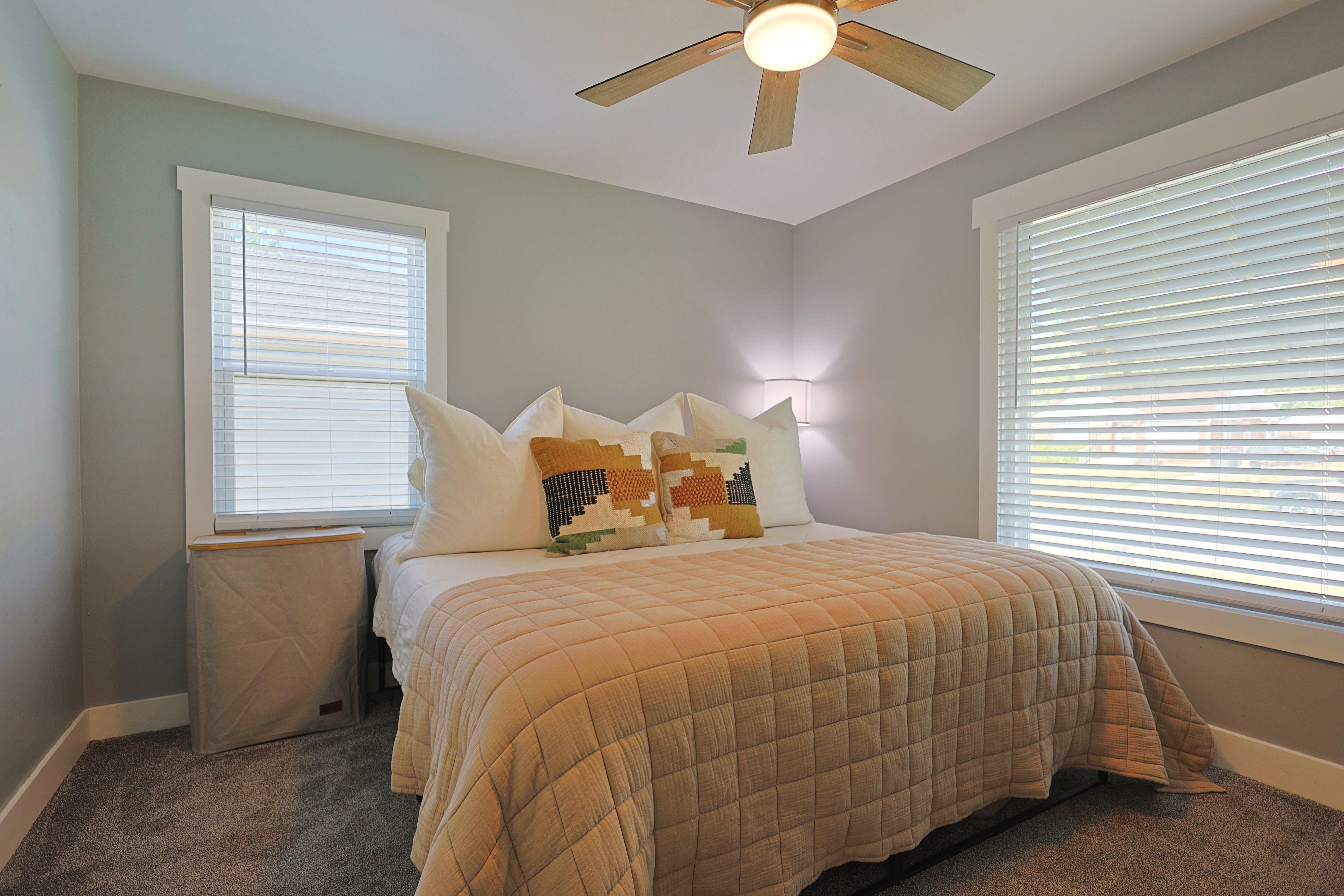 Carpeted room featuring a ceiling fan with integrated lighting, two windows with blinds, and white trim