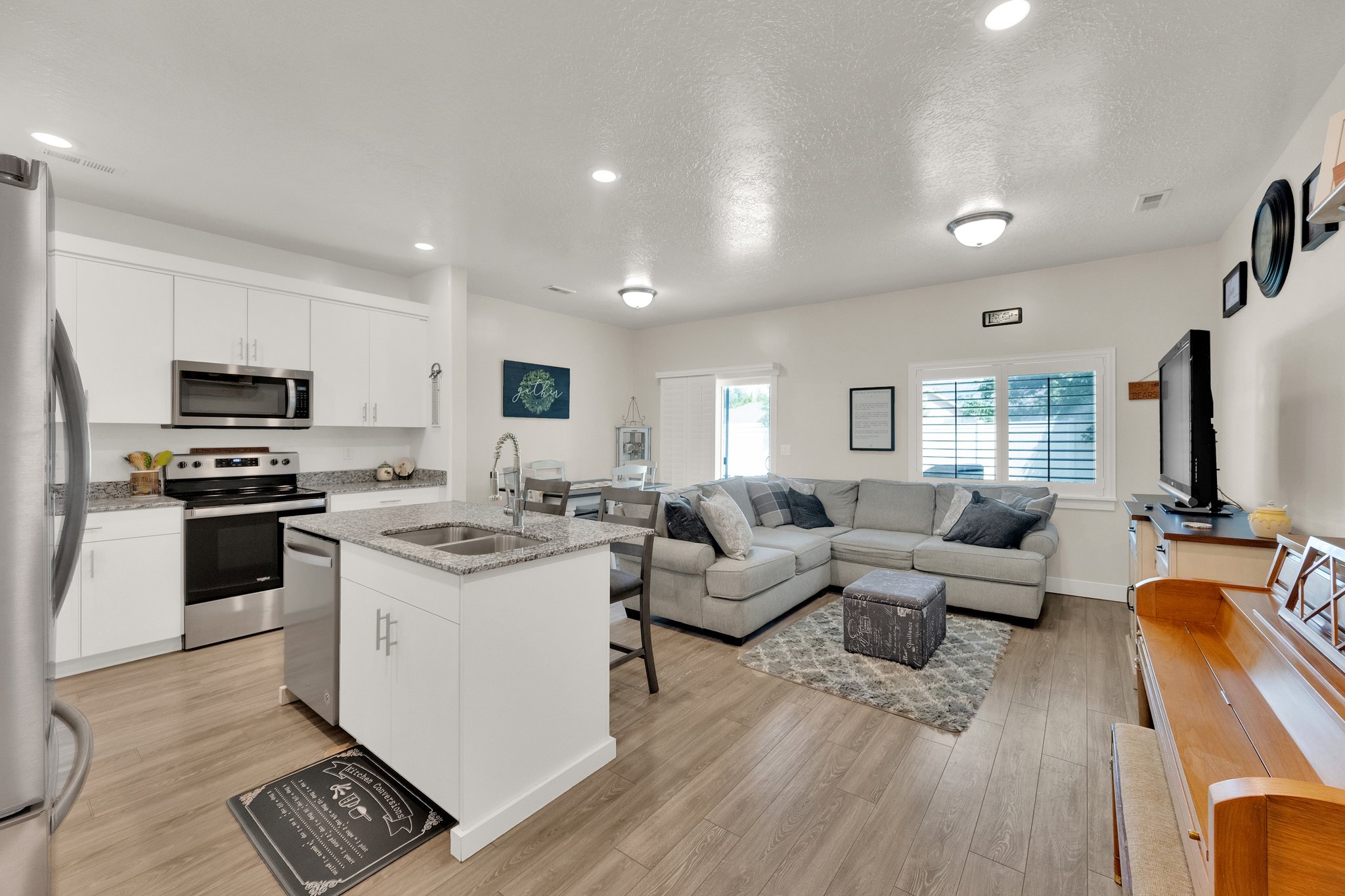 Open-concept living space featuring wood-finish flooring, recessed lighting, and a kitchen island with an undermount double sink