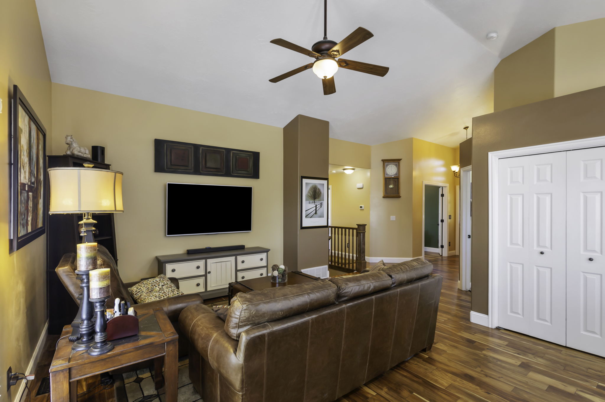 Vaulted ceiling with a wood-finish ceiling fan, hardwood flooring, built-in media console, and white bi-fold closet doors