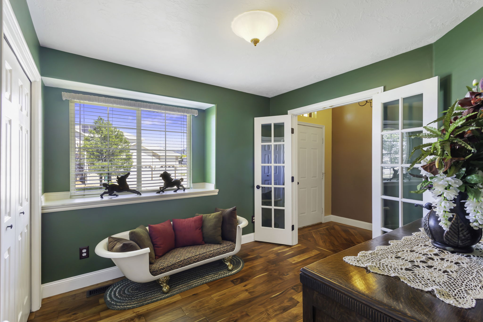 This flex space can be used as a formal living room, a bedroom, tv room, study etc.  It features  rich green walls, hardwood flooring, a large window with white trim  and lovely French doors.