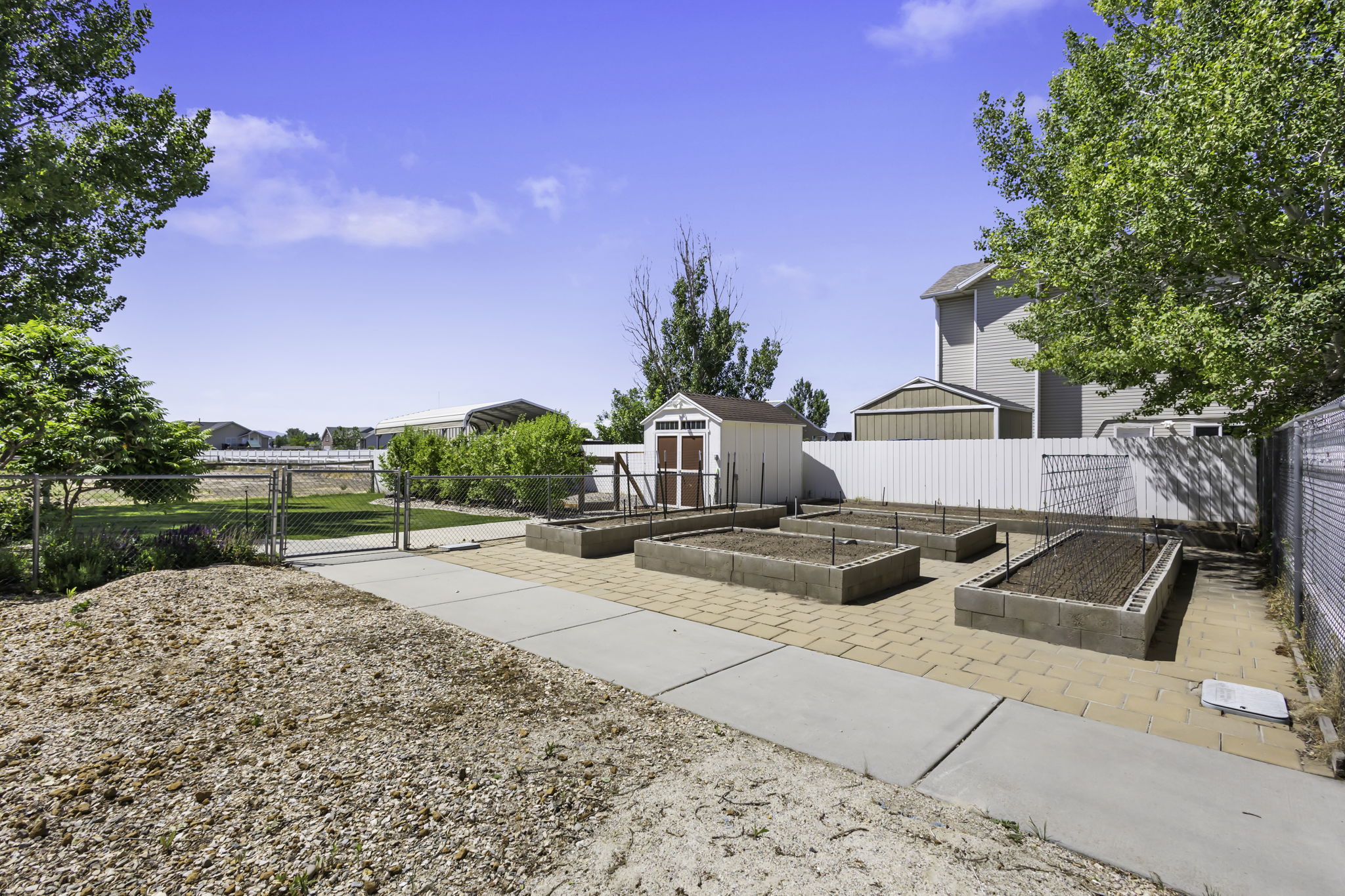 Backyard featuring four raised garden beds with watering system, concrete block construction,  storage shed., and a paver patio