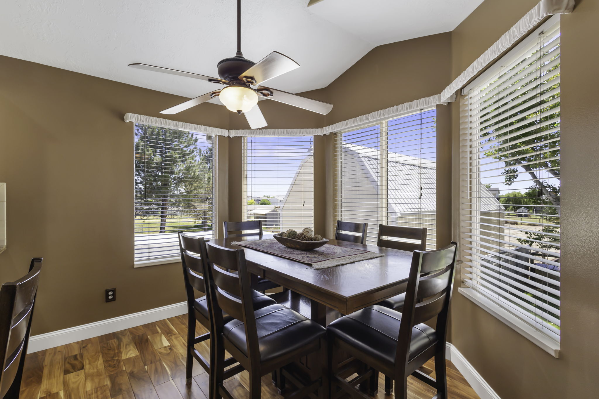 Dining area featuring hardwood  flooring, a contemporary ceiling fan with lighting, and multiple windows with horizontal blinds