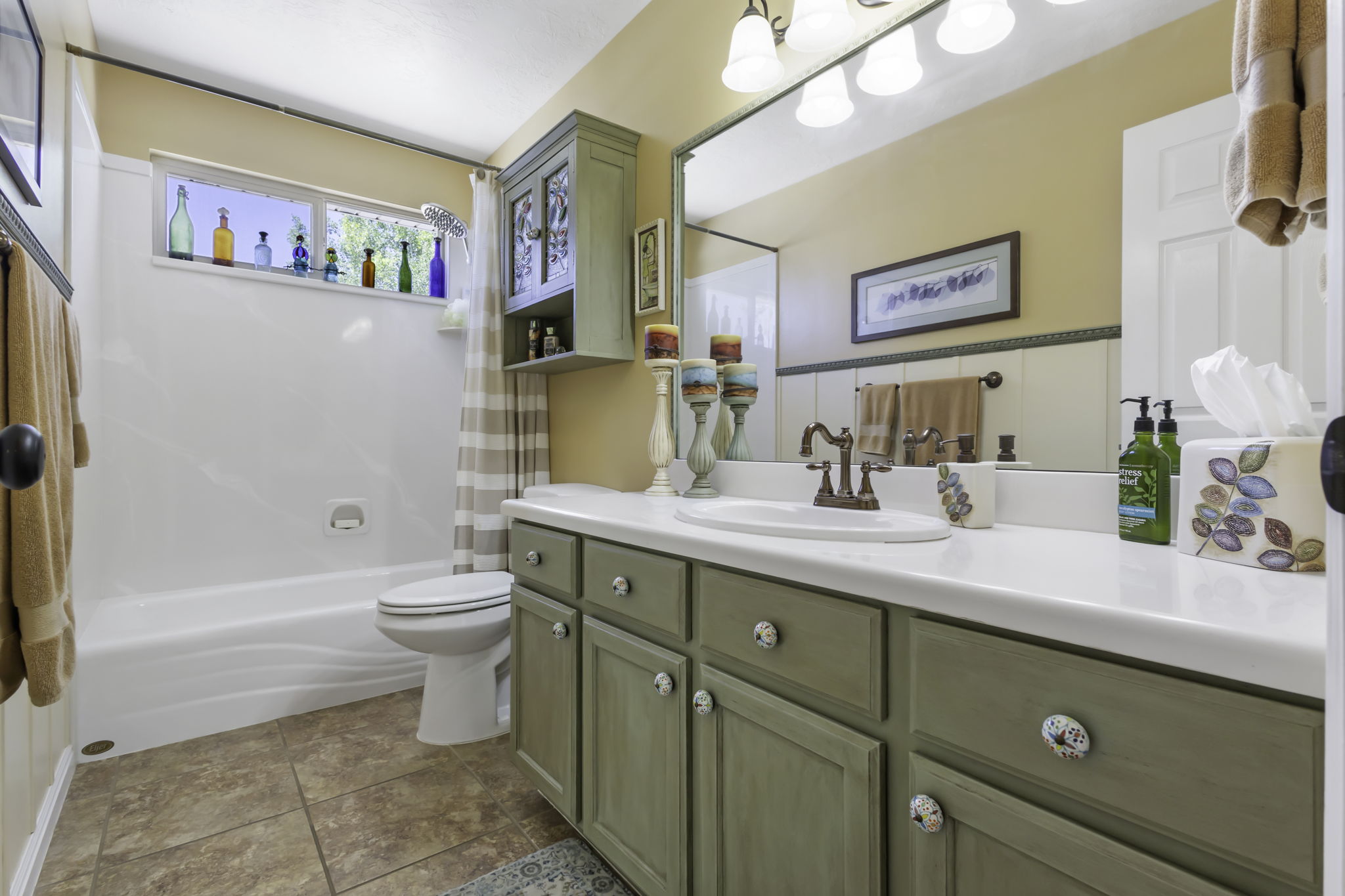 Bathroom featuring a single-basin vanity with a white countertop and sage green cabinetry, a built-in tub with a shower, and tile flooring