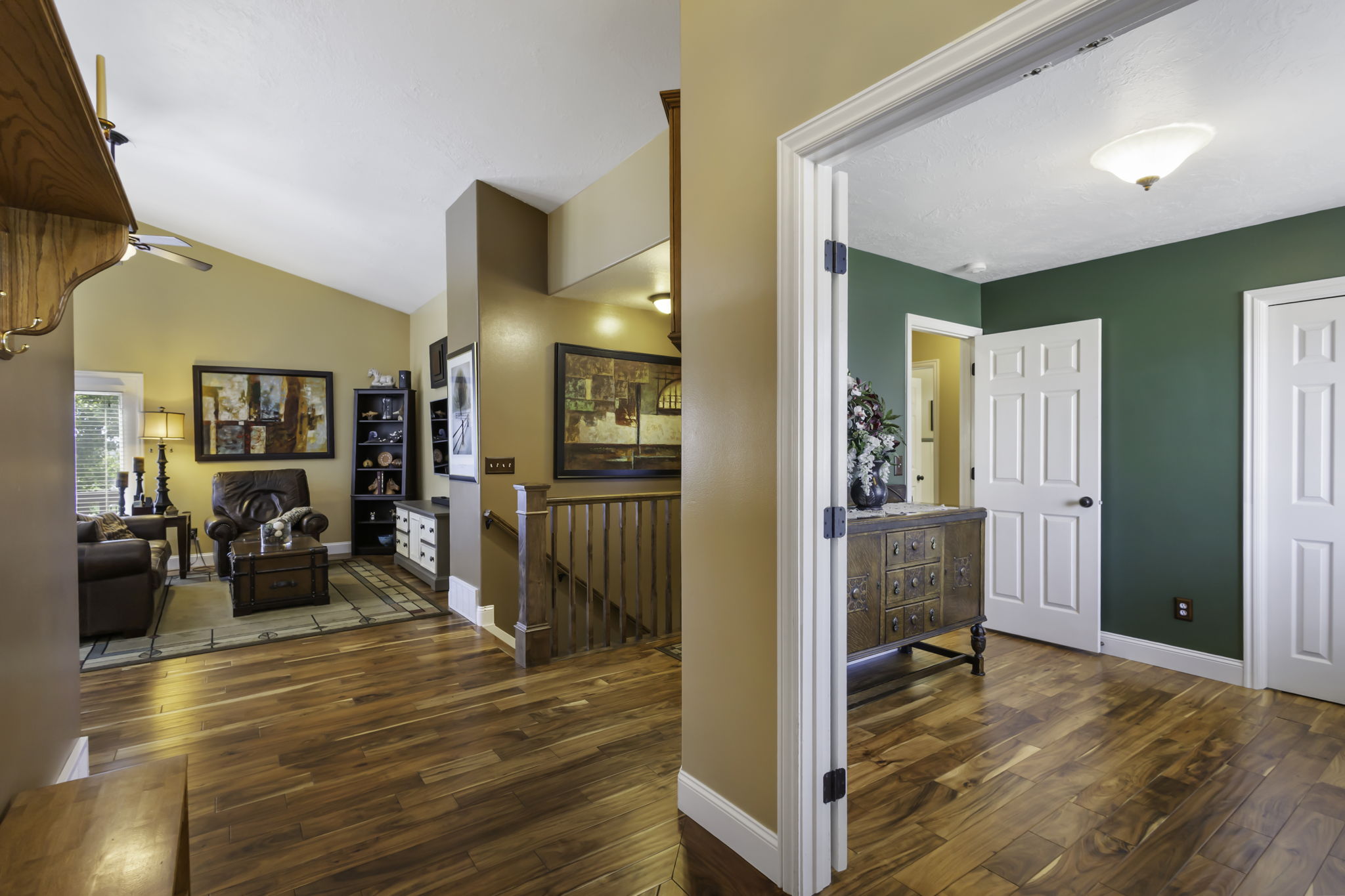 Open-concept foyer featuring hardwood flooring, leading to the living room with a vaulted ceiling, and  staircase with a wood railing leading to the basement