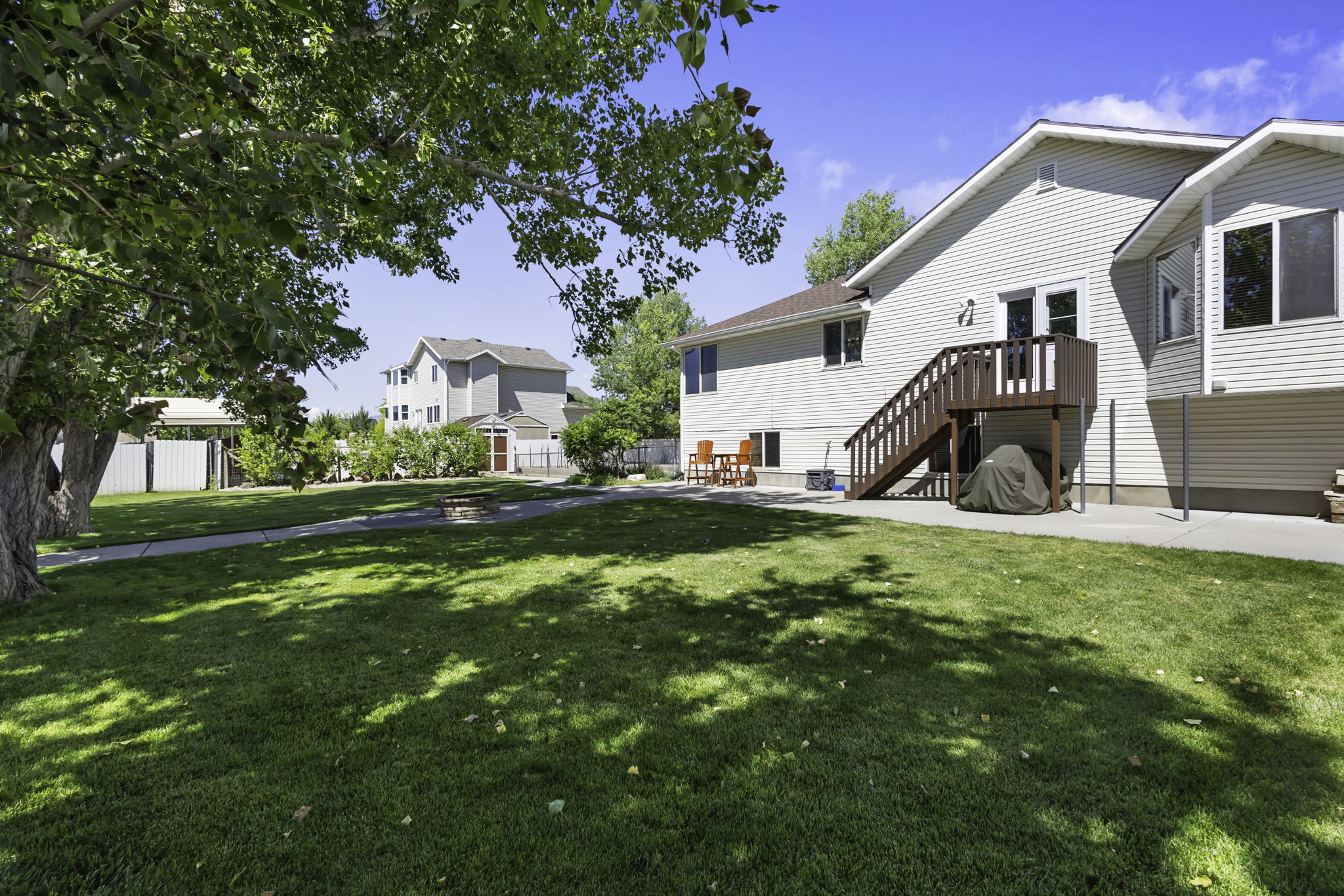 Spacious backyard featuring a manicured lawn, established trees, and a built-in fire pit