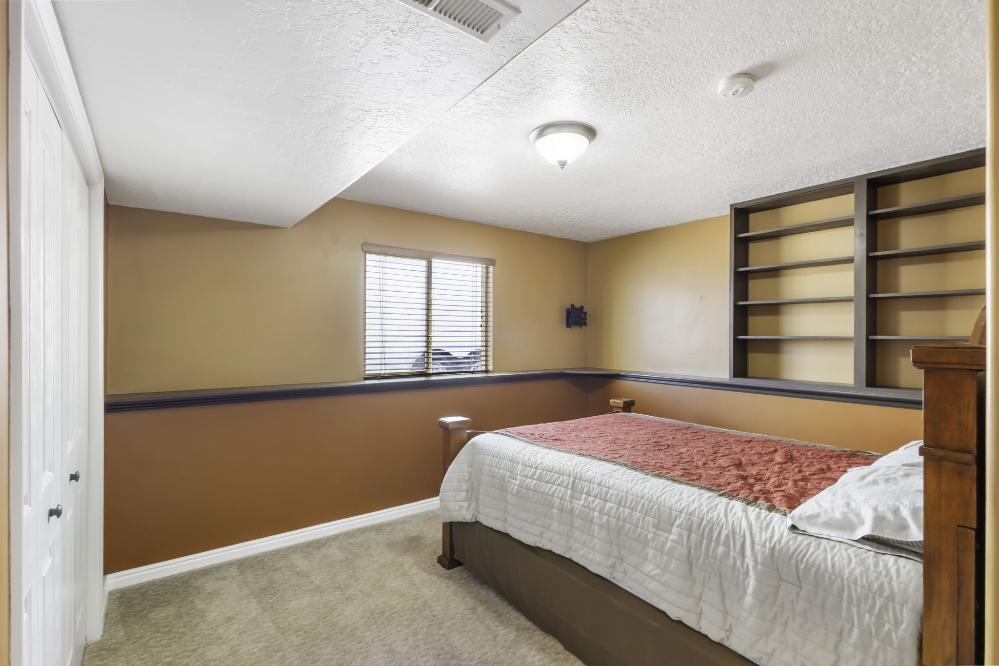 Bedroom featuring built-in shelving, a window with blinds, wall-to-wall carpeting, and a built-in closet with bi-fold doors