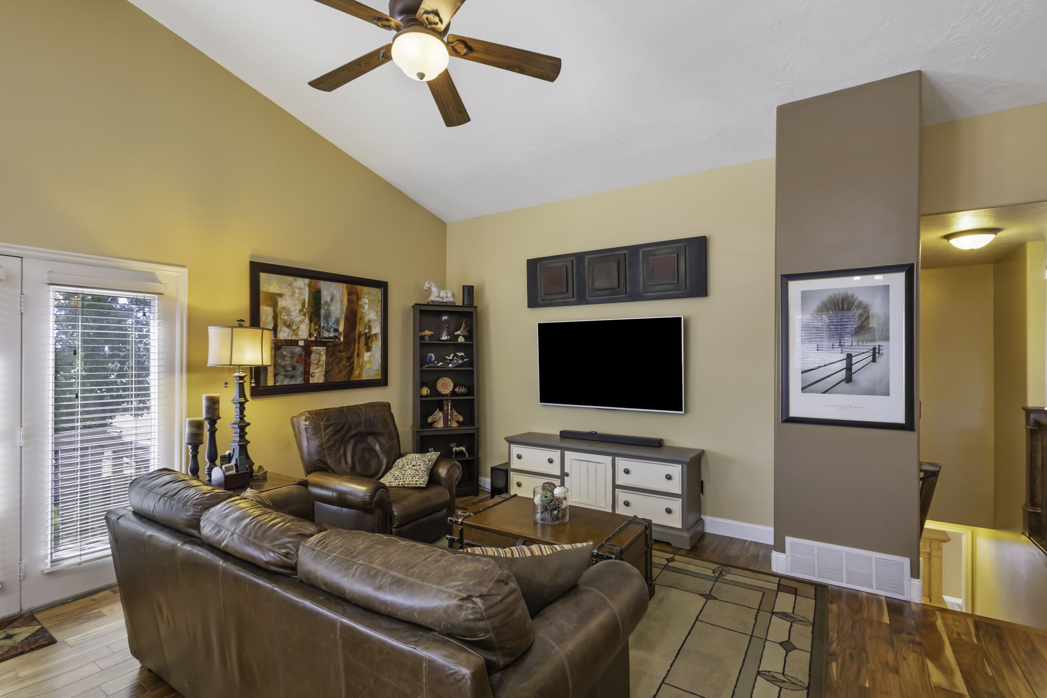 Living area featuring vaulted ceilings, a ceiling fan with integrated lighting, hardwood flooring, and double glass-paned doors