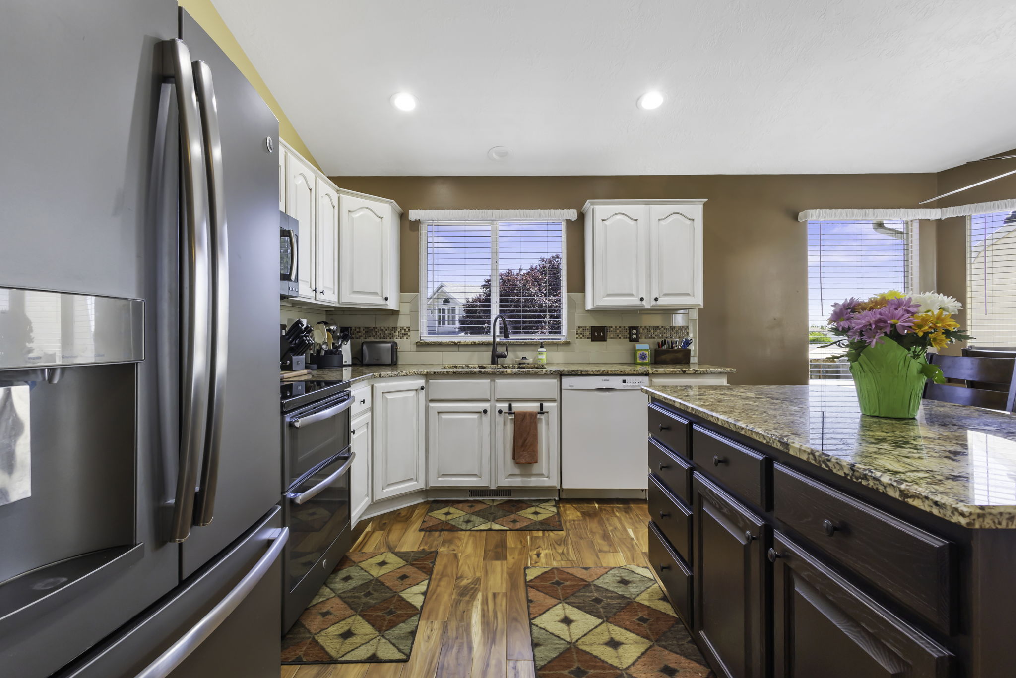 Kitchen, featuring integrated stainless steel appliances, white cabinetry, granite countertops, and hardwood flooring
