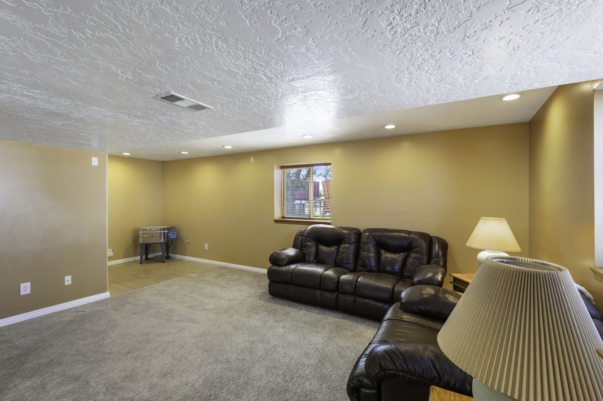 Spacious lower-level family  room featuring recessed lighting, a daylight window with wood trim, and a combination of carpeted and tiled flooring