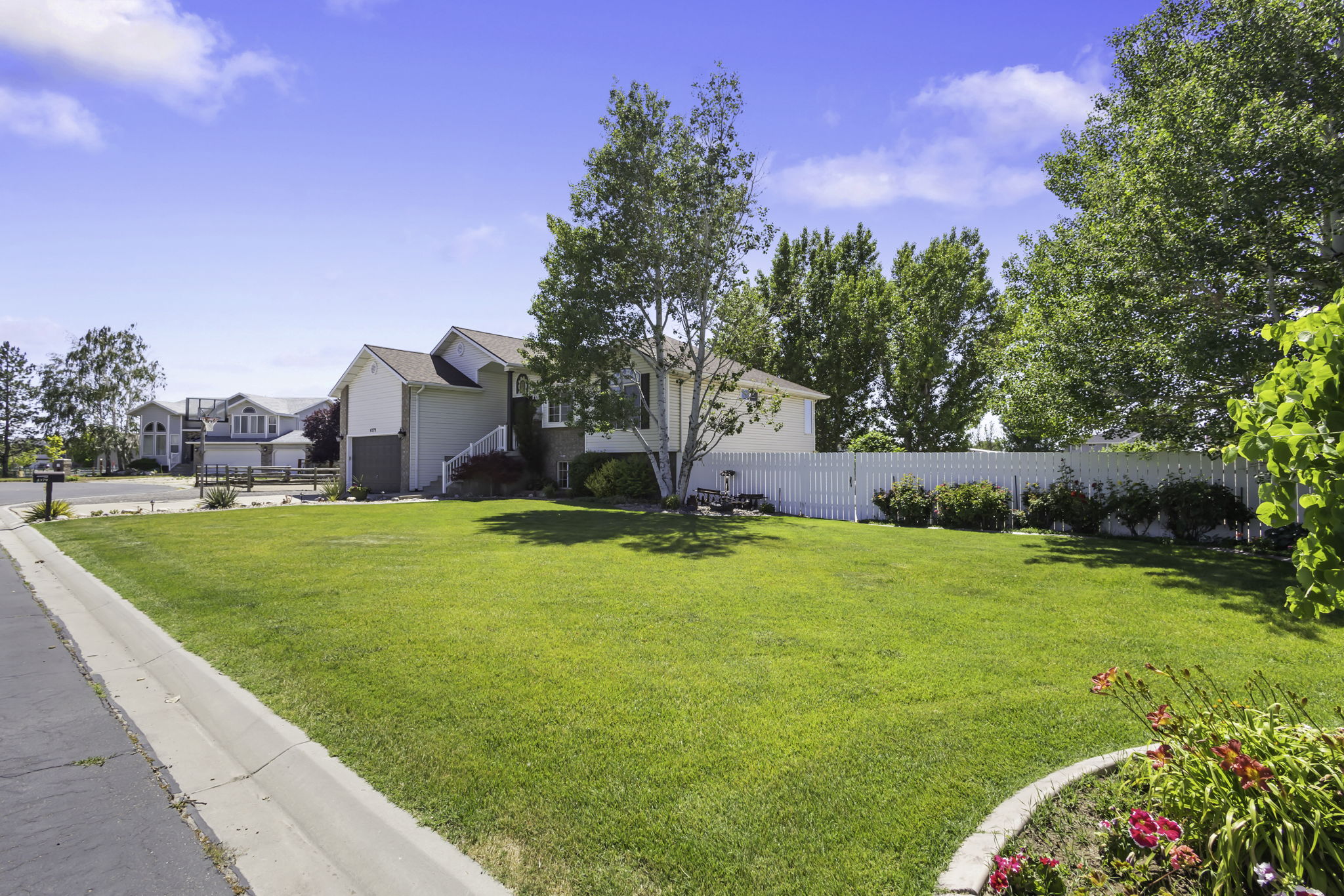 Spacious front yard with a manicured lawn, featuring eye catching flowers, exterior lighting, mature trees, and a concrete driveway.
