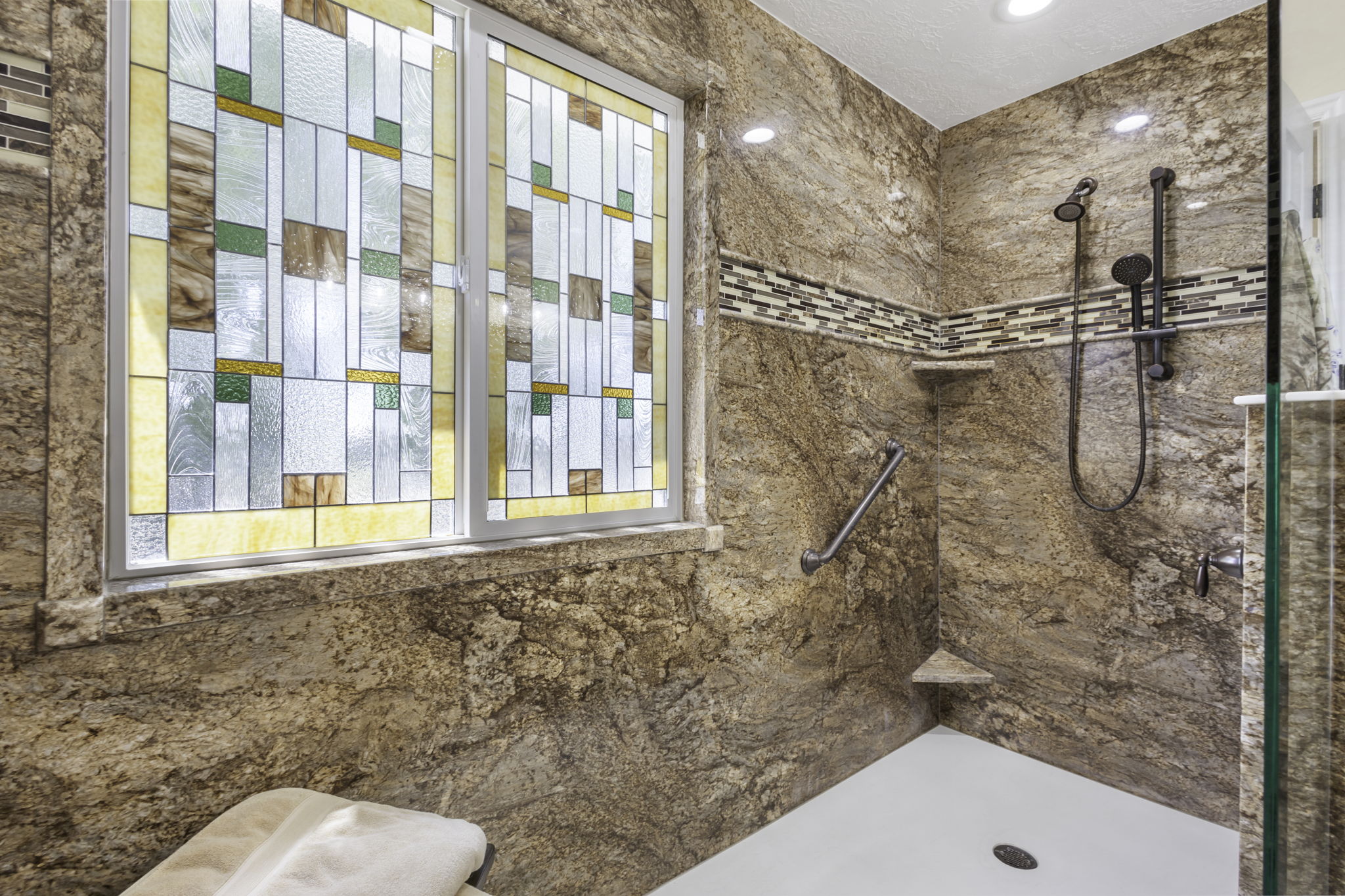 Shower enclosure featuring full-height stone-finish walls, a decorative mosaic tile accent band, a built-in corner shelf, and an integrated grab bar