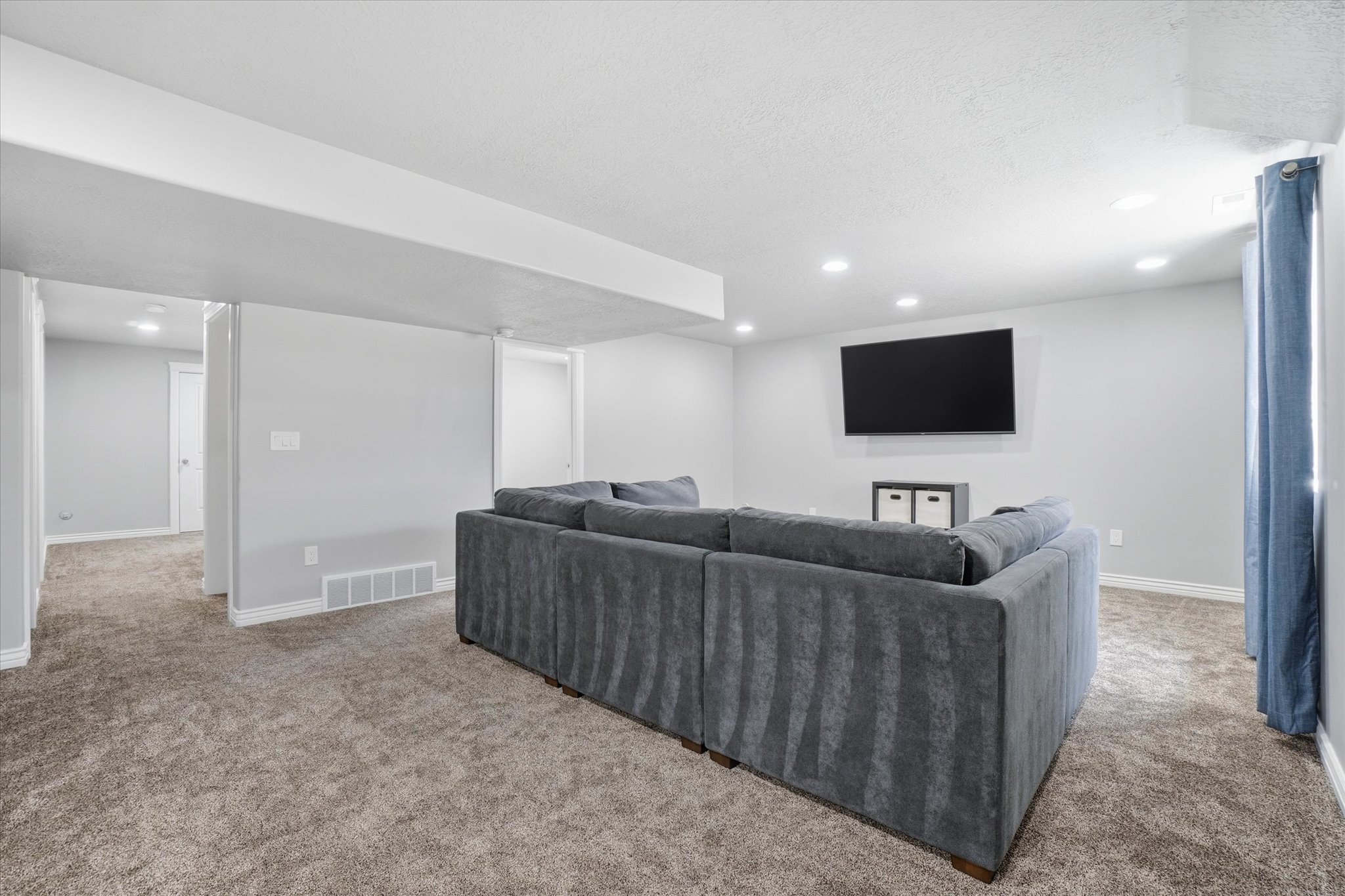 Spacious entertainment area featuring recessed lighting, a mounted media display, and neutral carpeting