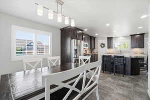 Open-concept kitchen and dining area featuring dark wood-finish cabinetry, stainless steel appliances, and a stone-finish countertop