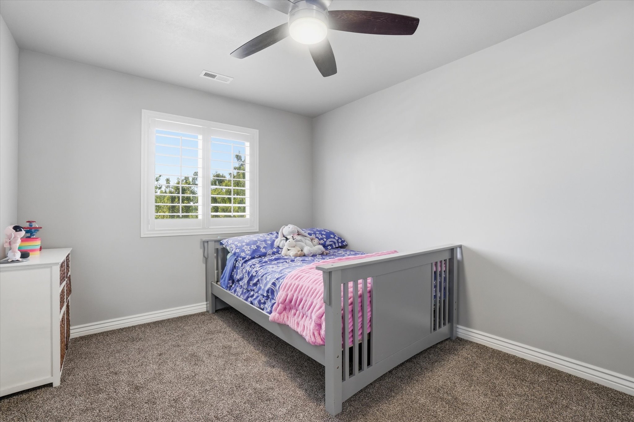 Room featuring neutral wall tones, carpeted flooring, a window with white louvered shutters, and a ceiling fan with integrated lighting