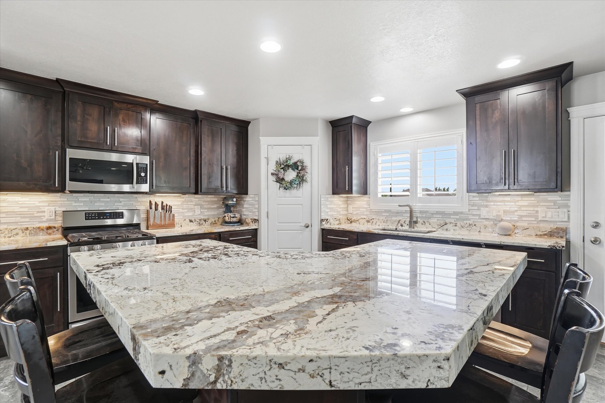 Spacious kitchen featuring a large island with a substantial countertop, dark wood-finish cabinetry, stainless steel appliances, a tile backsplash, and recessed lighting
