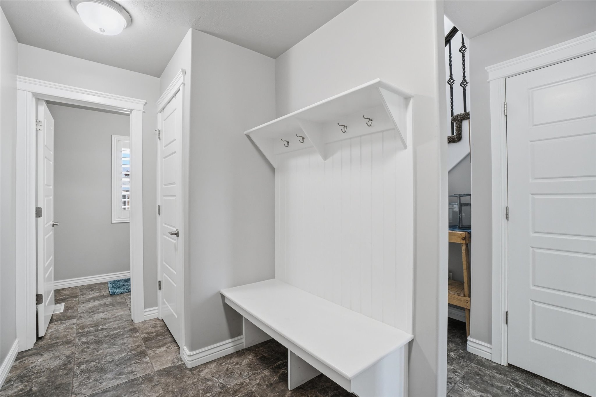 Built-in white bench with coat hooks and beadboard backing, set against light gray walls