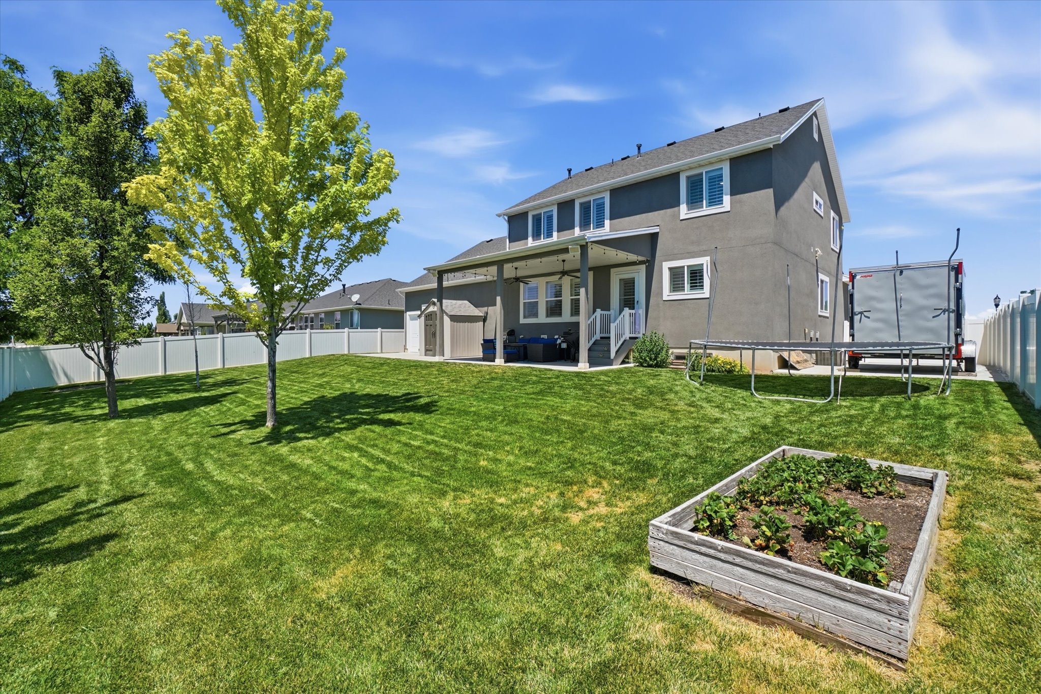 Spacious backyard featuring an expansive lawn, mature trees, and a raised garden bed